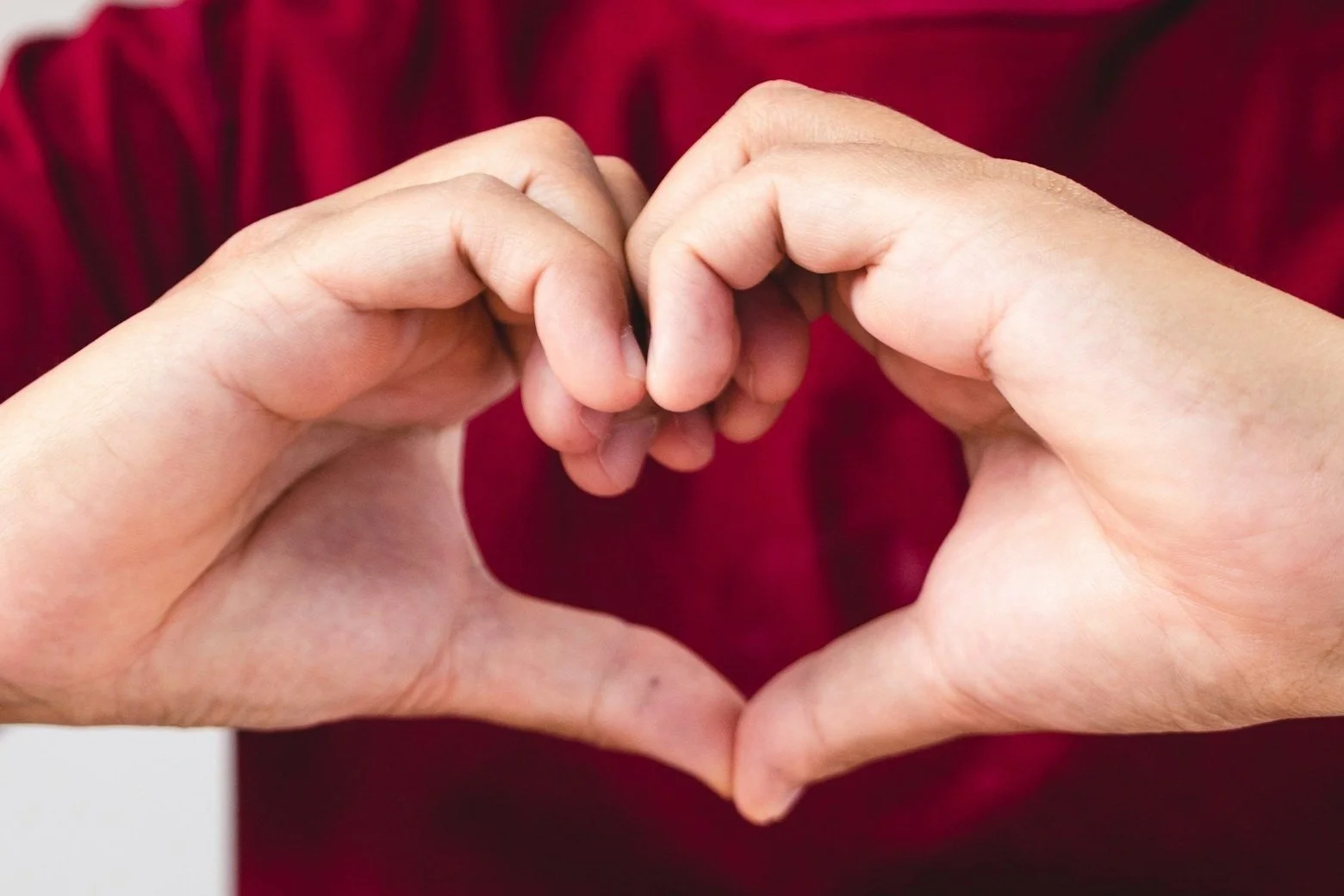 Two hands forming a heart shape against a red background.