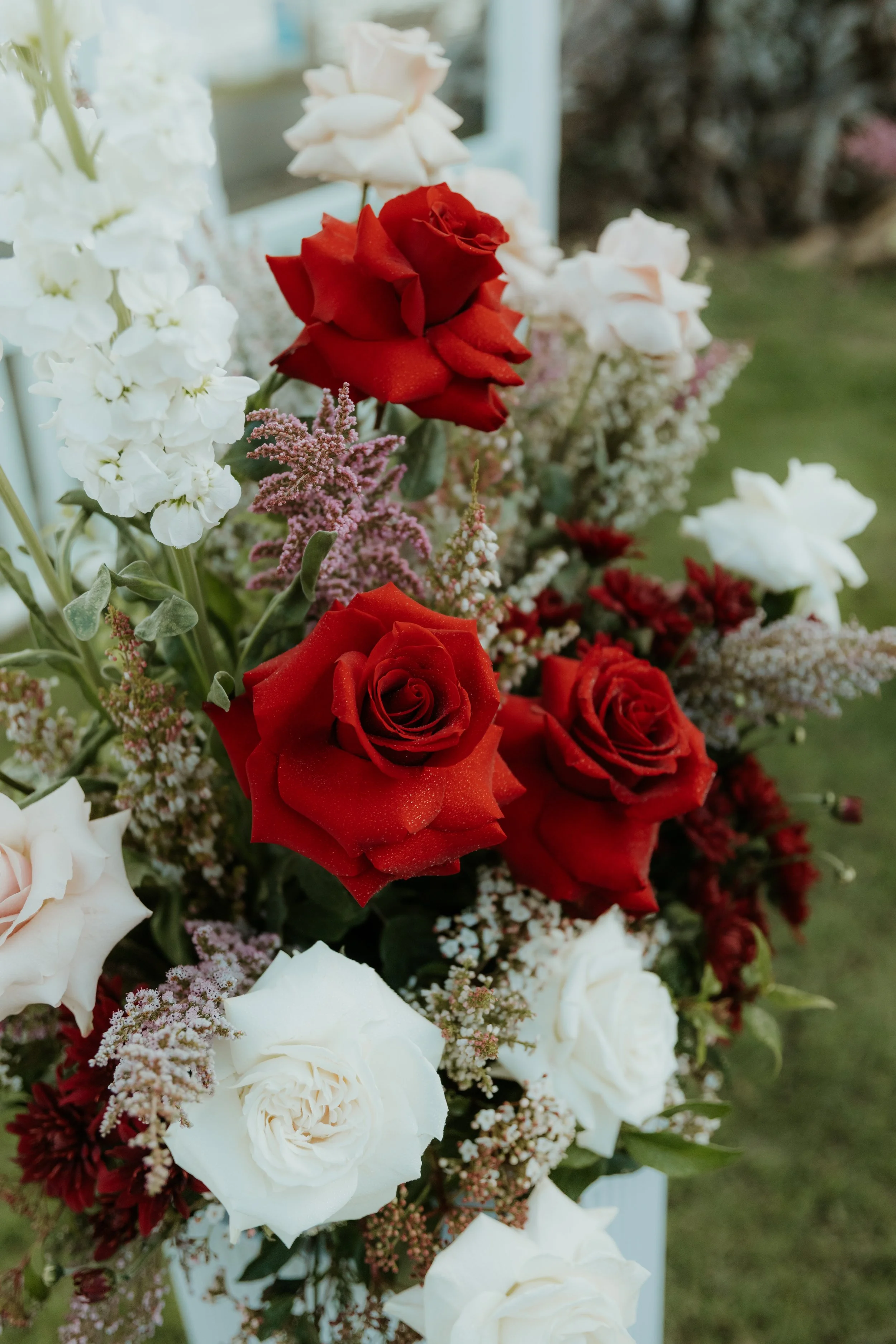 A bouquet of mixed red and white roses with small pink and white filler flowers, set outdoors.