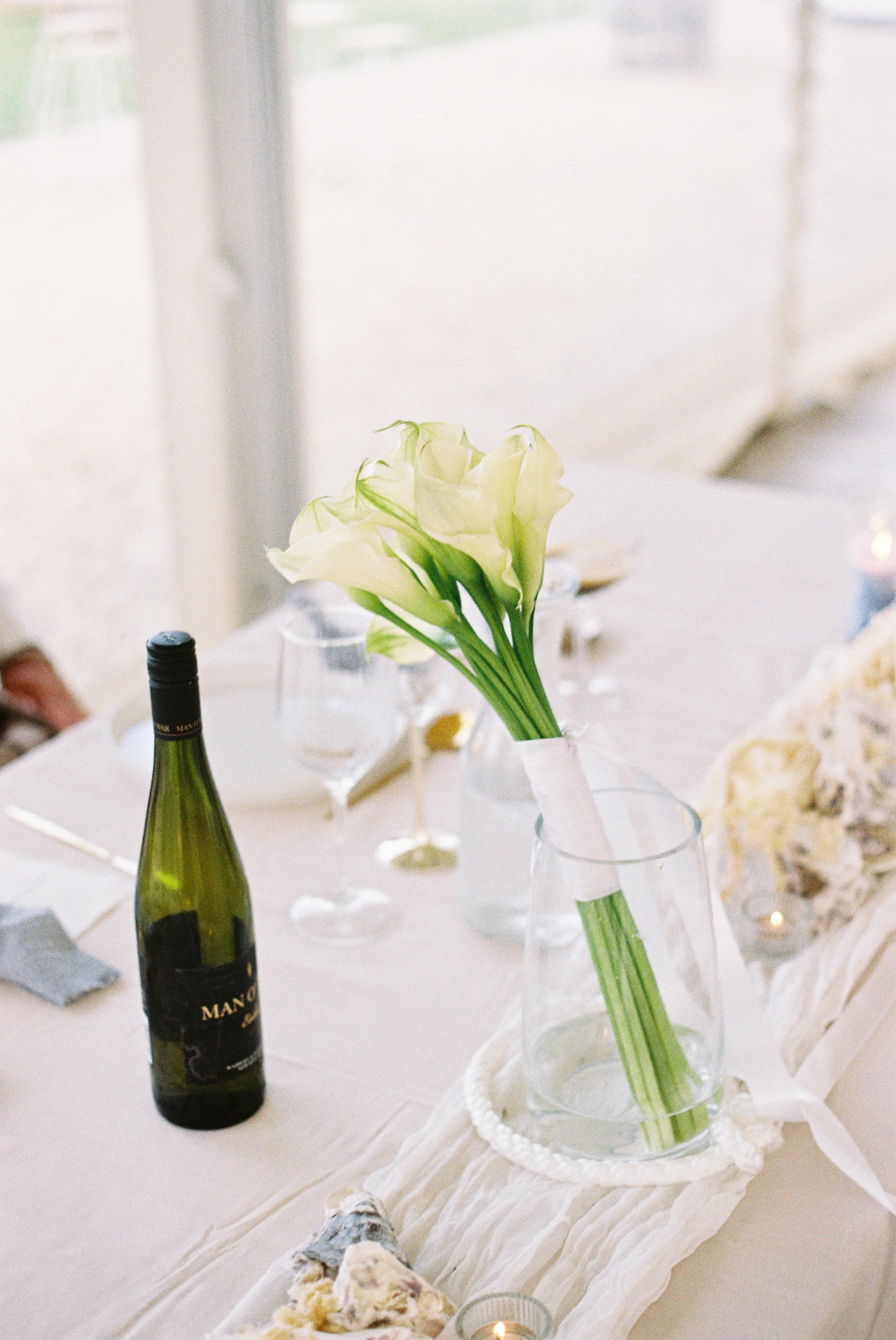 A table decorated with a white floral centerpiece, bottles of wine, and desserts, set for a celebration or gathering.