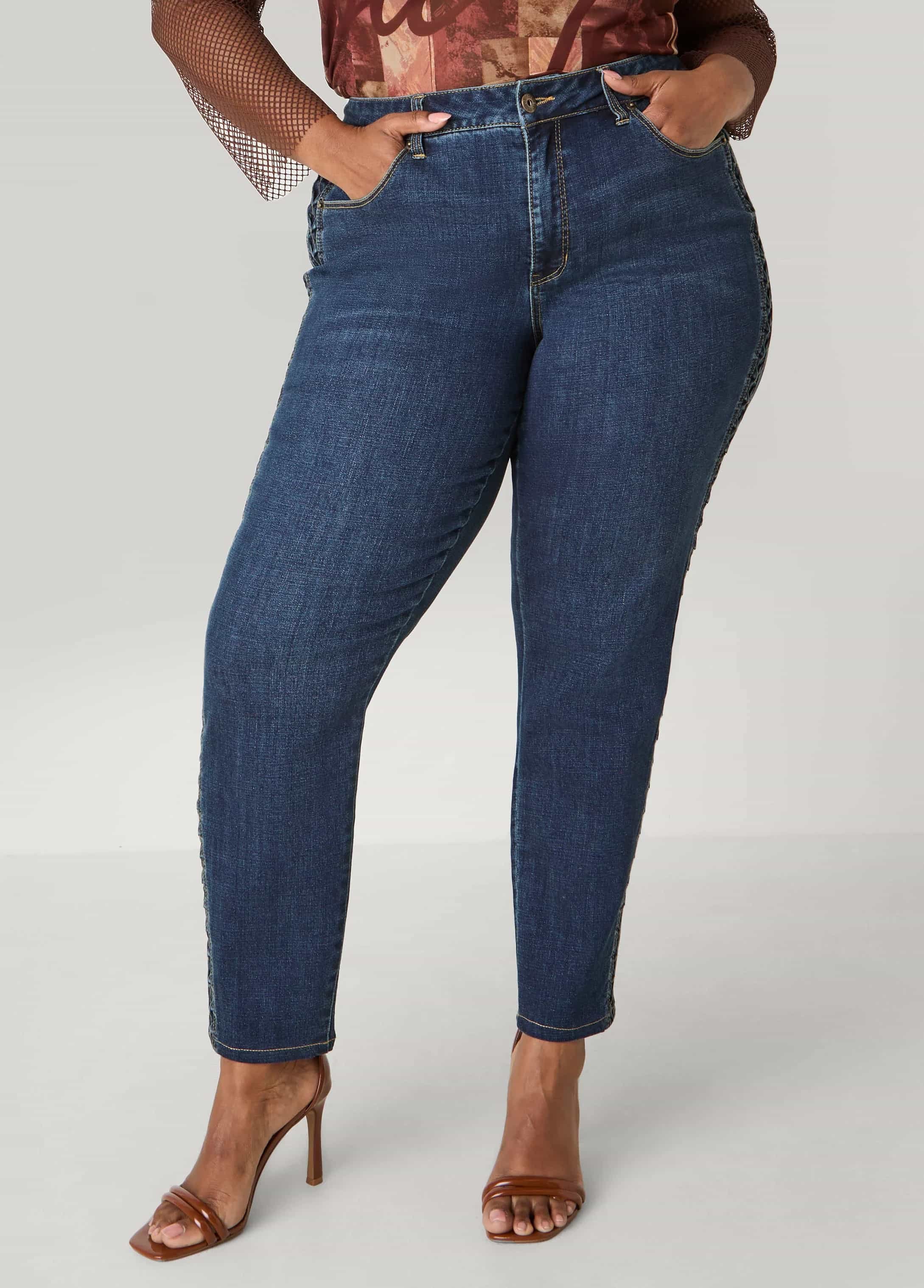 Model wearing high-waisted dark blue jeans designed by Keagan Roberson - styled with a graphic top and brown heels, hands in pockets for a relaxed pose.