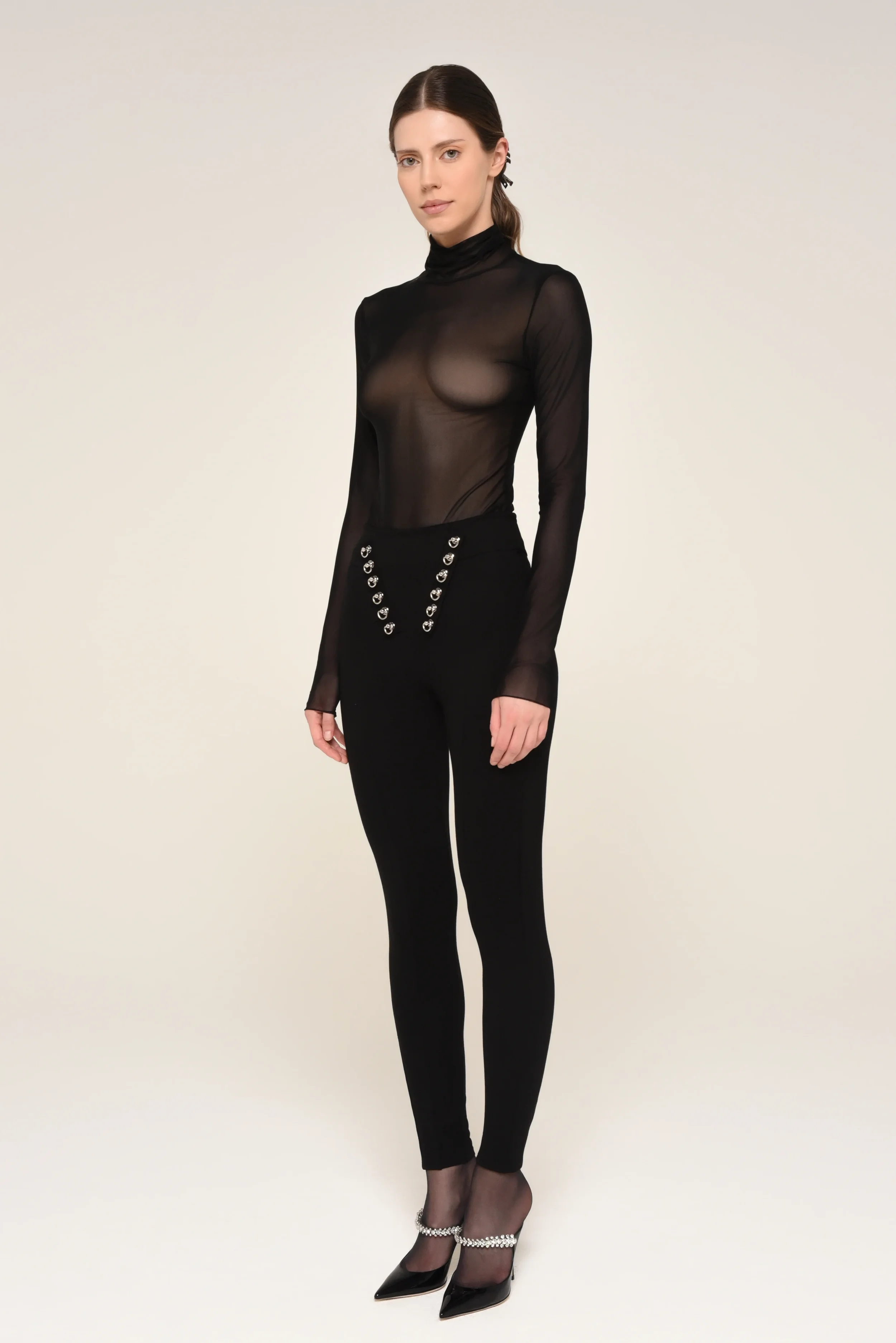 Model wearing a sheer black long-sleeve top and embellished black pants with pearl-detailed heels - designed in collaboration with Keagan Roberson.