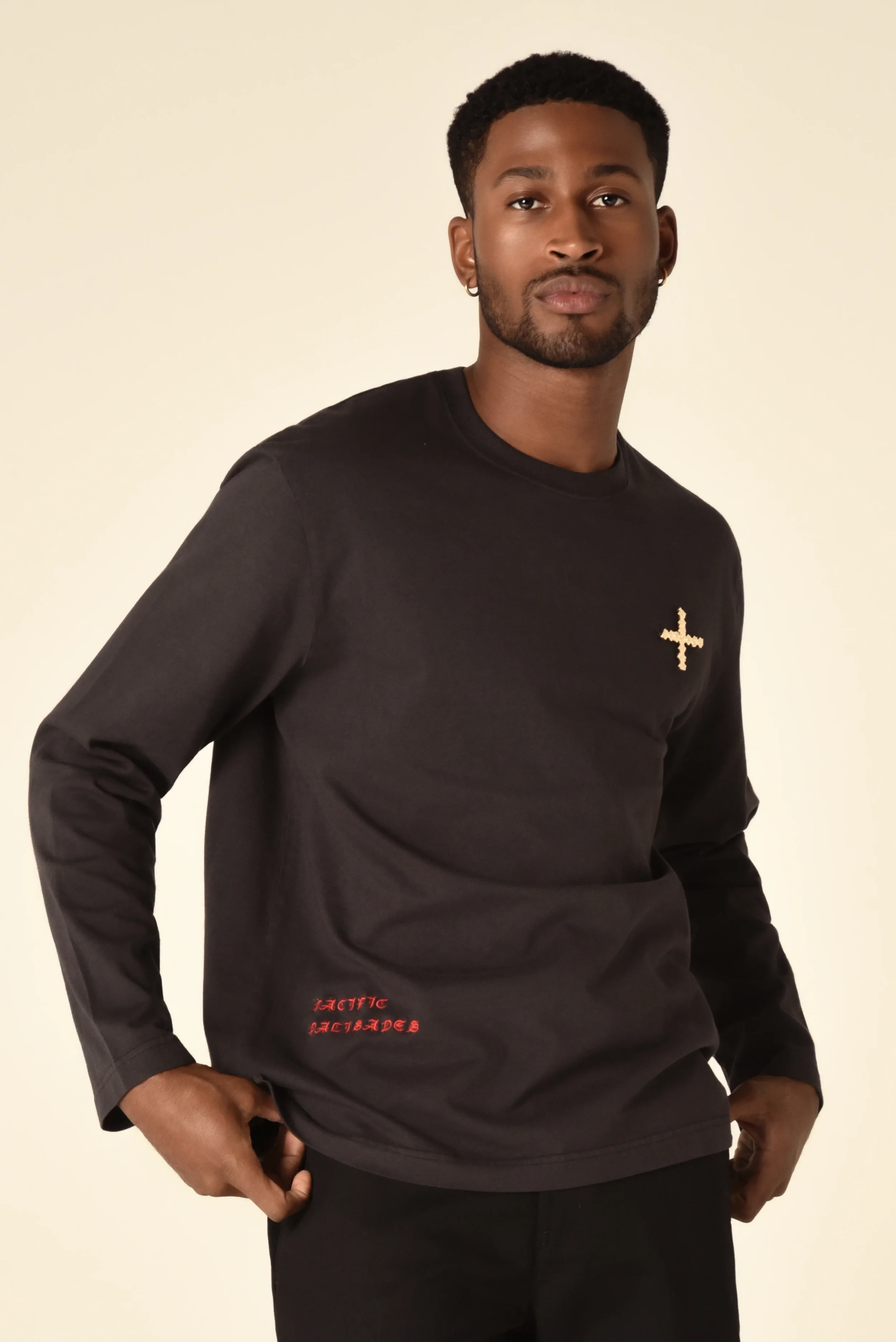 Model wearing a black long-sleeve shirt with an embroidered cross on the chest and red text detail - designed in collaboration with Keagan Roberson for Seymone.