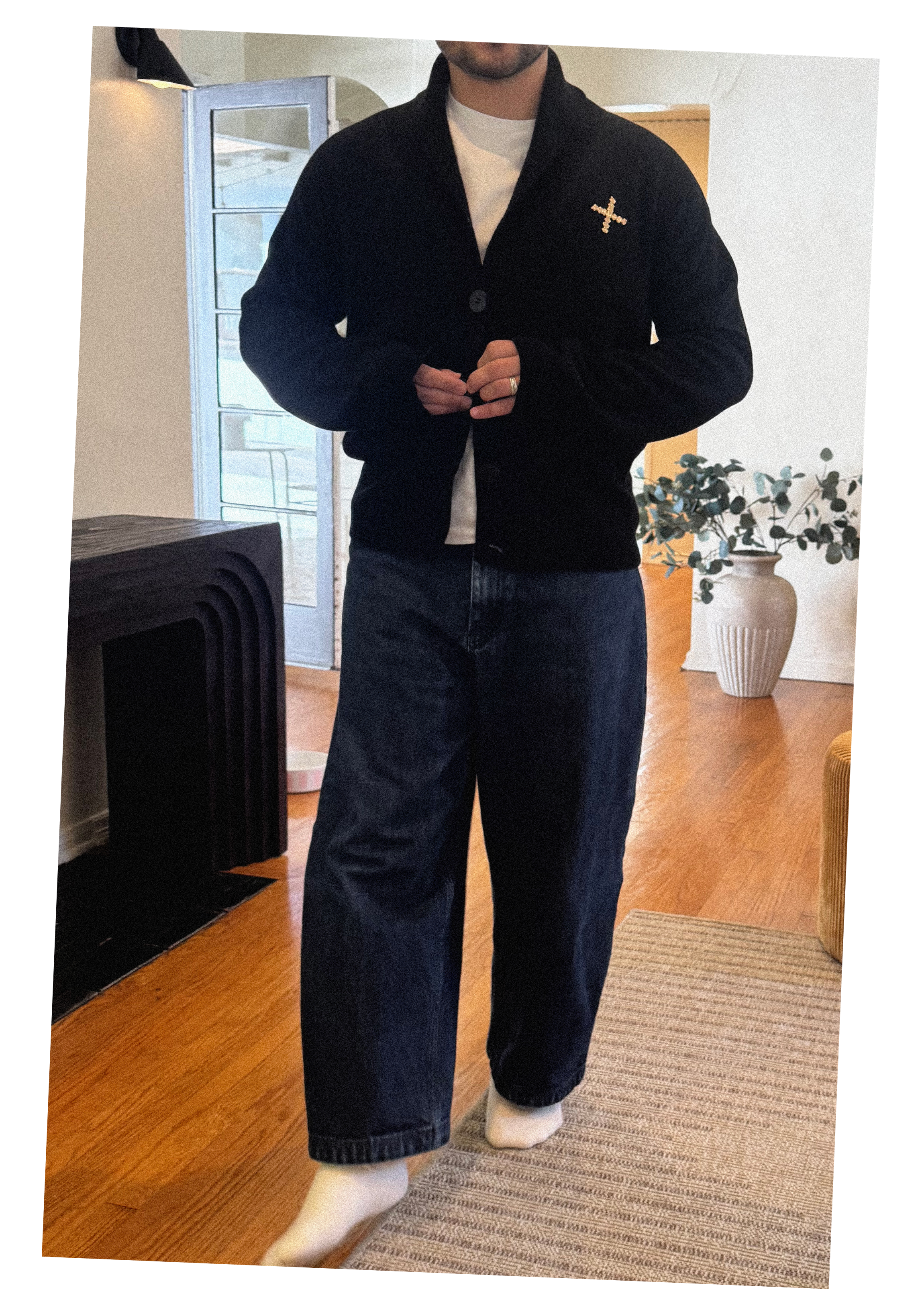 Keagan Roberson wearing a black jacket with a cross pin layered over a white shirt and dark denim.