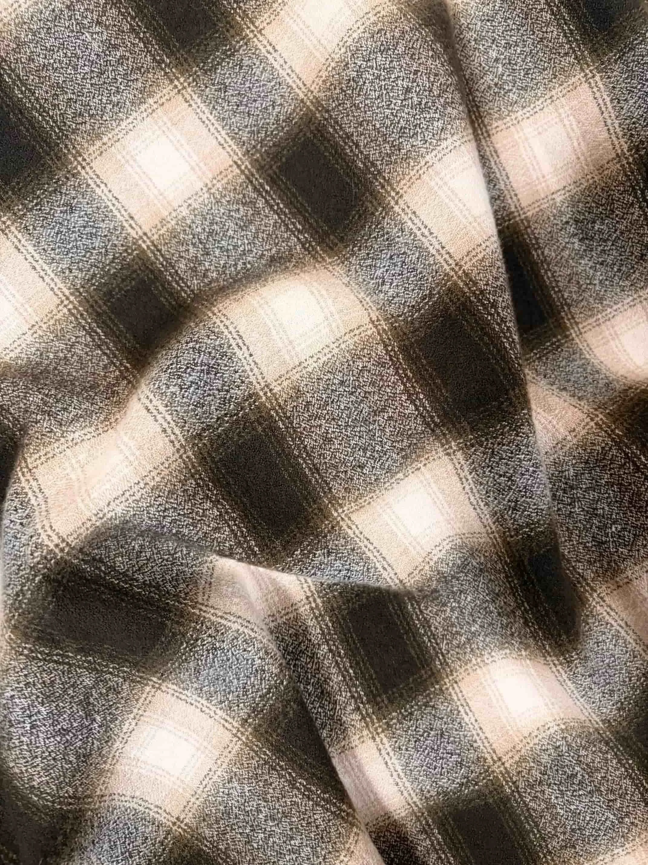 Close-up of a piece of fabric with a plaid pattern in shades of brown, black, and beige, showing folds and texture.