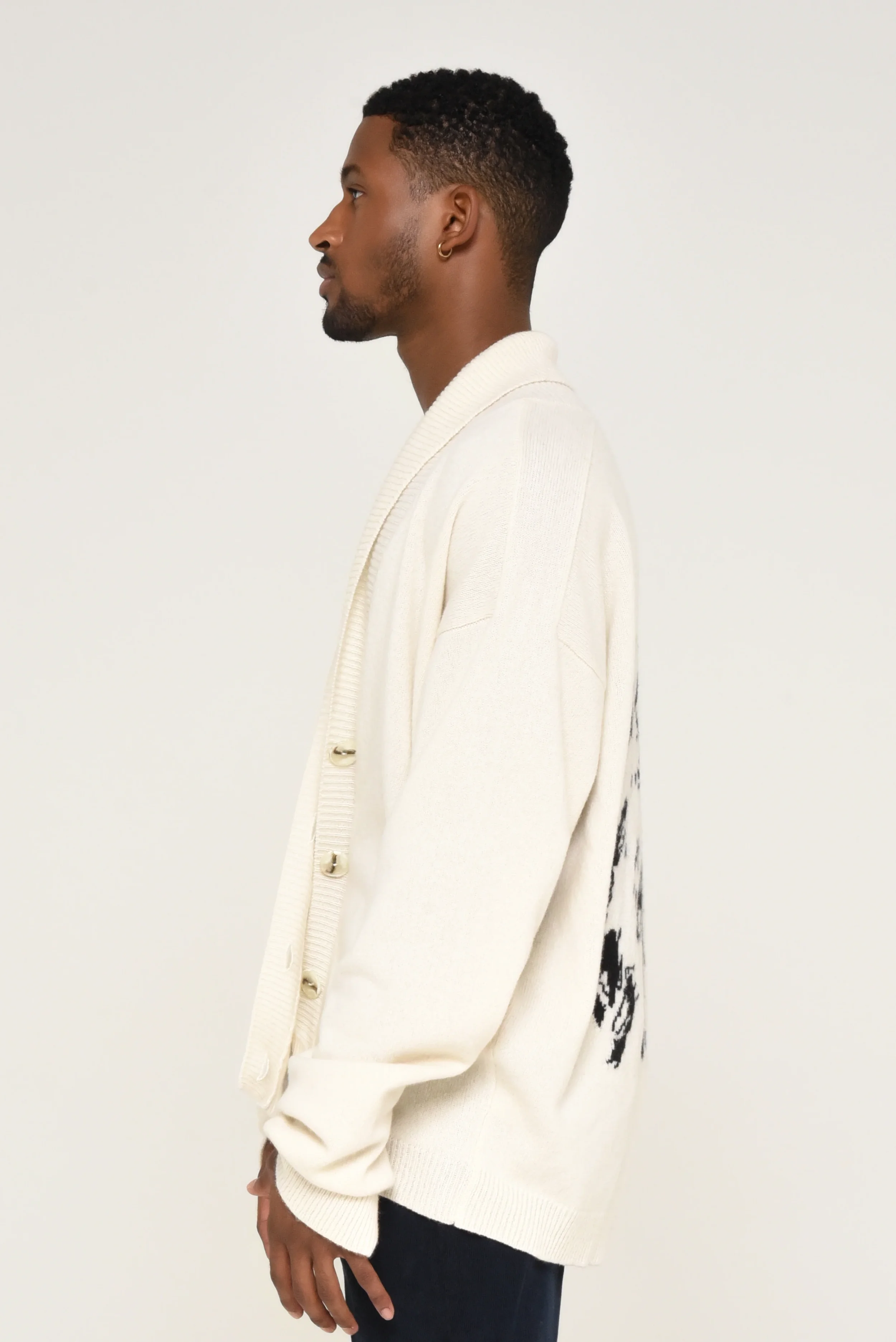 Side view of a model wearing a beige cardigan and dark trousers - designed in collaboration with Keagan Roberson.