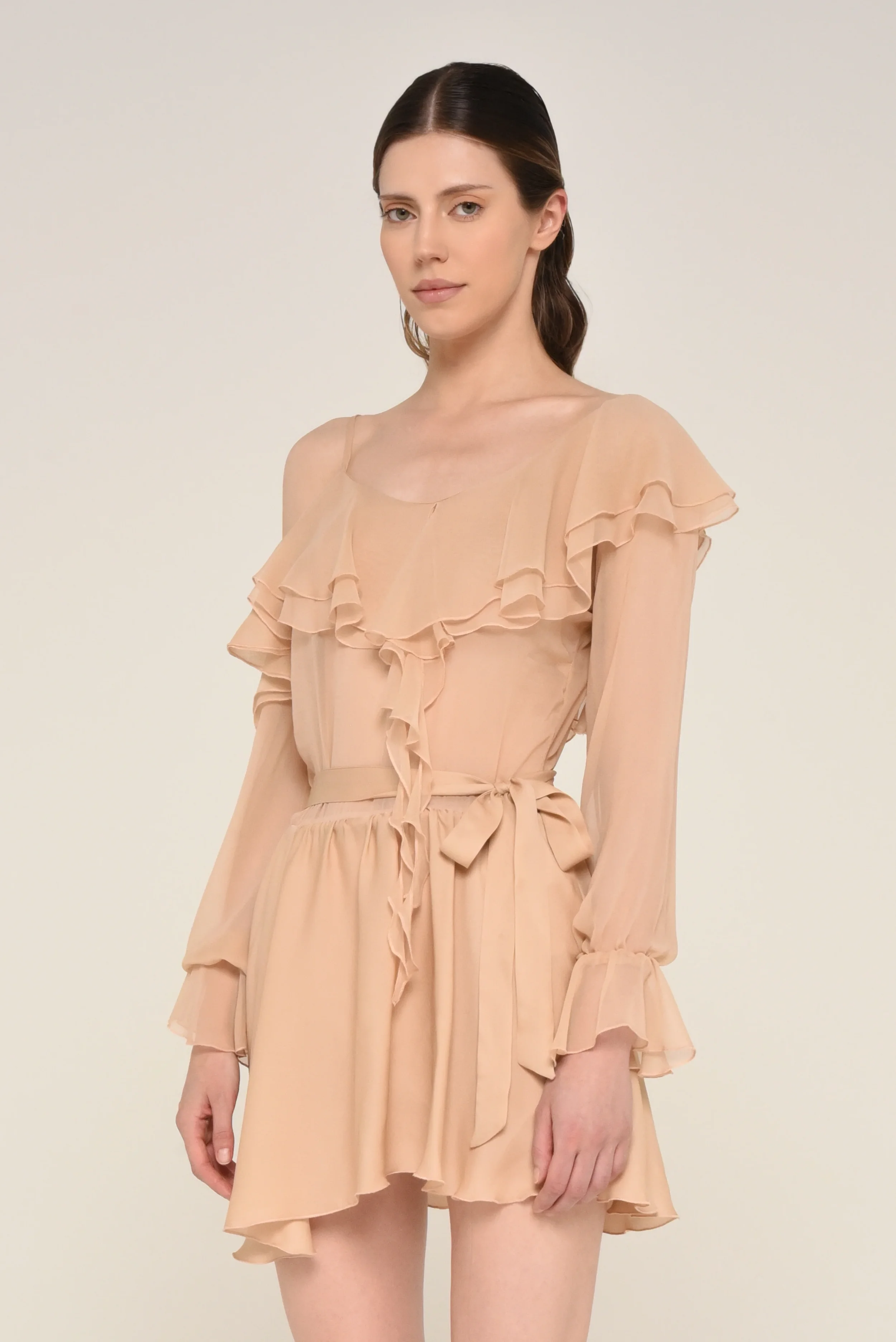 Model wearing a nude ruffled long-sleeve dress with a waist tie - designed in collaboration with Keagan Roberson.