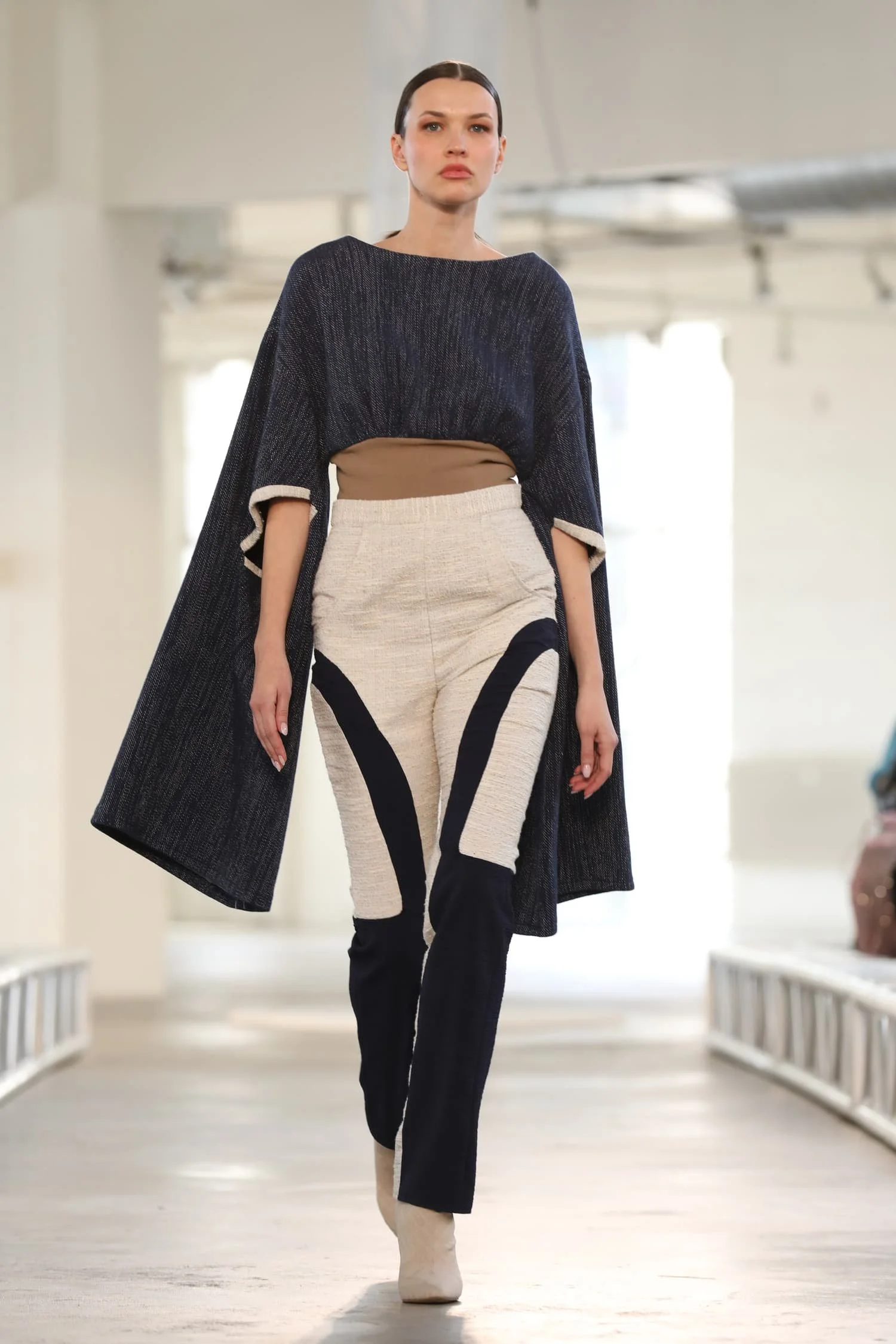 Model walking on runway in black and beige designer outfit at fashion show. Keagan Roberson collection.