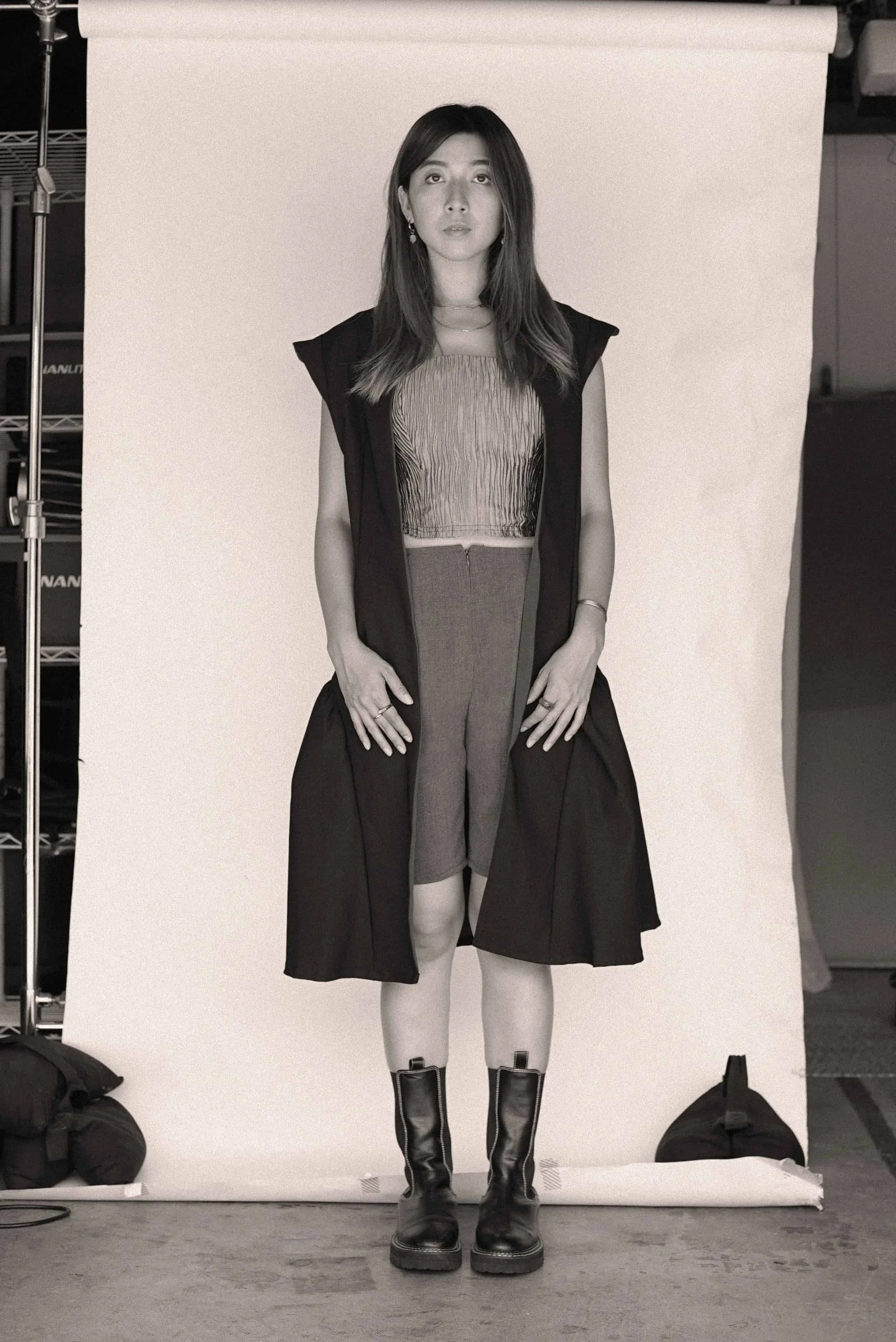 Model wearing a sleeveless top, tailored shorts, and long coat from Keagan Roberson - structured look styled with combat boots in studio.