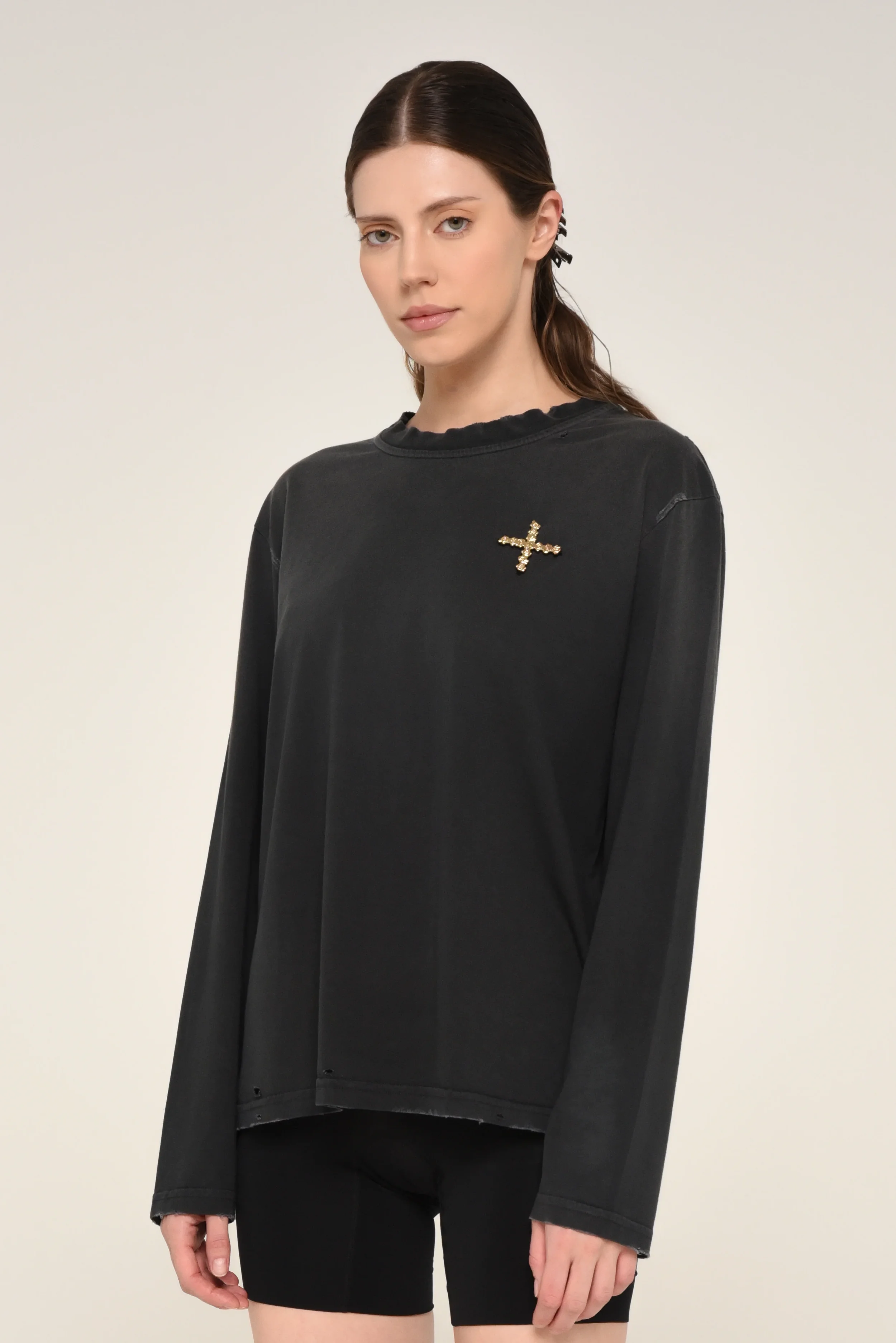 Model wearing a black long-sleeve shirt with a gold cross brooch on the chest - designed in collaboration with Keagan Roberson.
