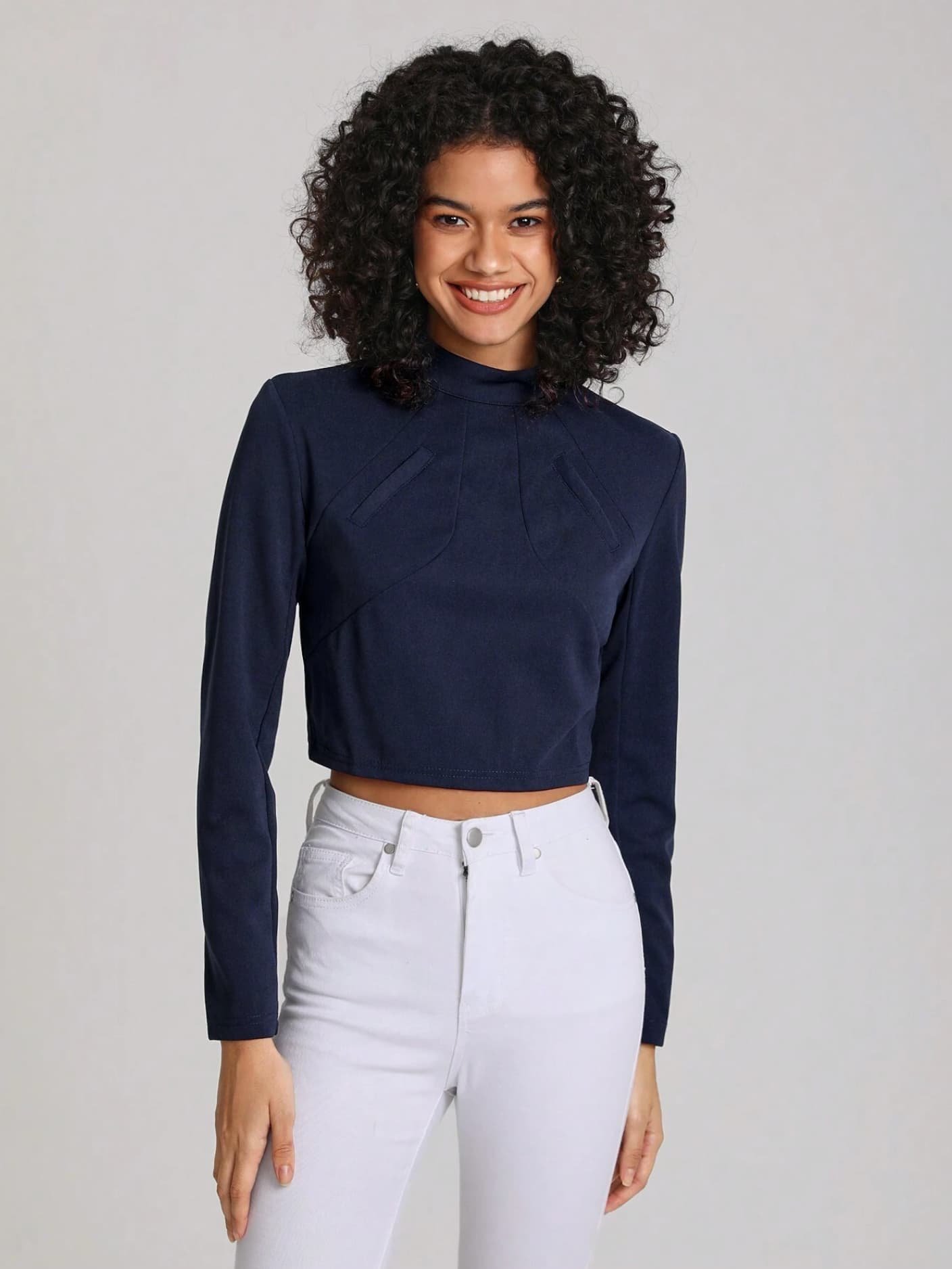 Model with curly hair wearing a navy long-sleeve crop top and white denim from Keagan Roberson - minimal portrait against a soft gray backdrop.