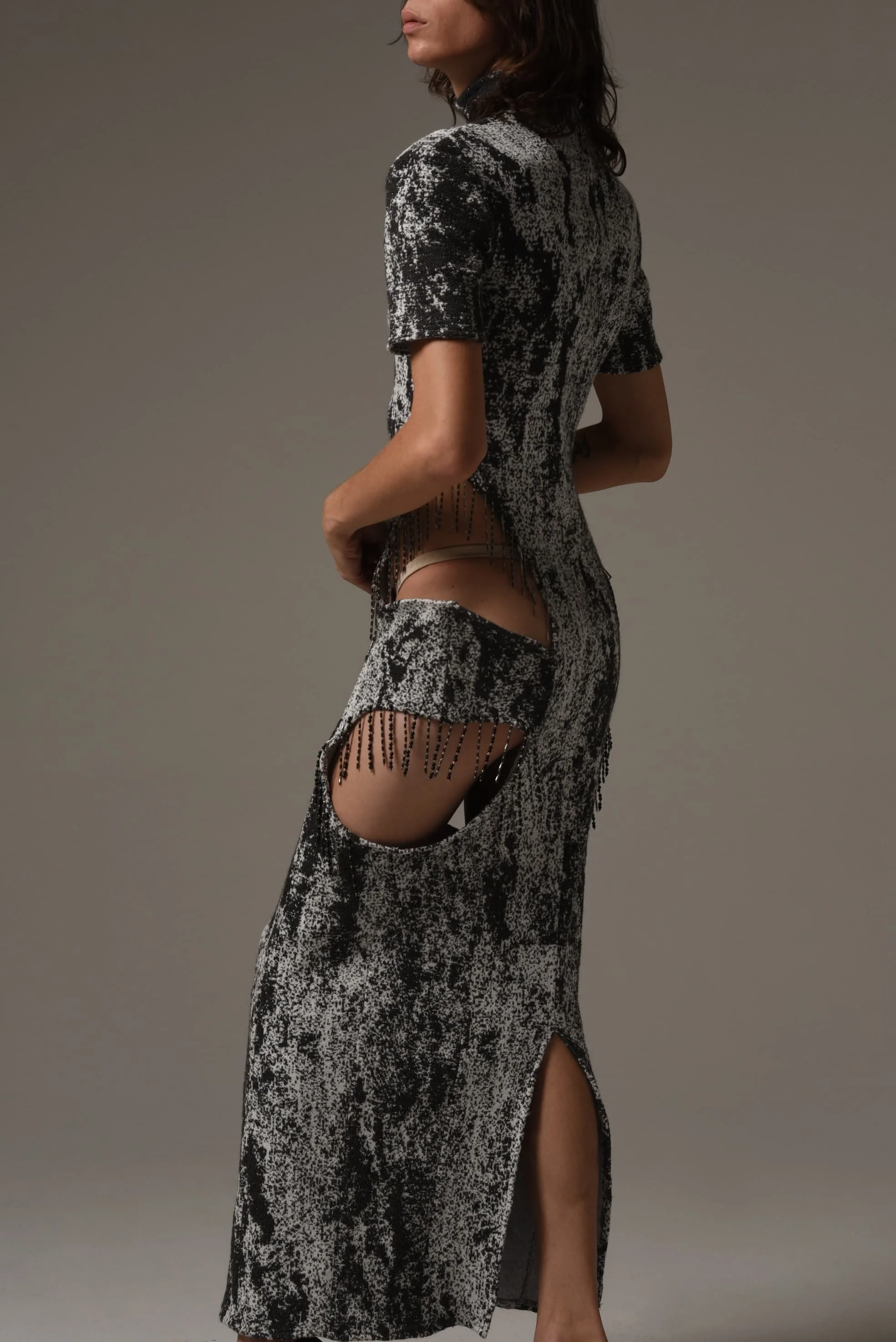 Model wearing a black-and-white patterned dress with fringe and cutout detailing from Keagan Roberson - styled against a neutral gray backdrop.