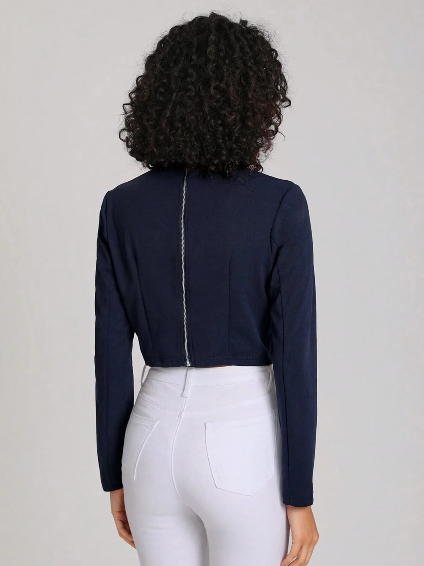 Back view of a model wearing a navy cropped jacket and white jeans from Keagan Roberson - clean studio composition highlighting silhouette.