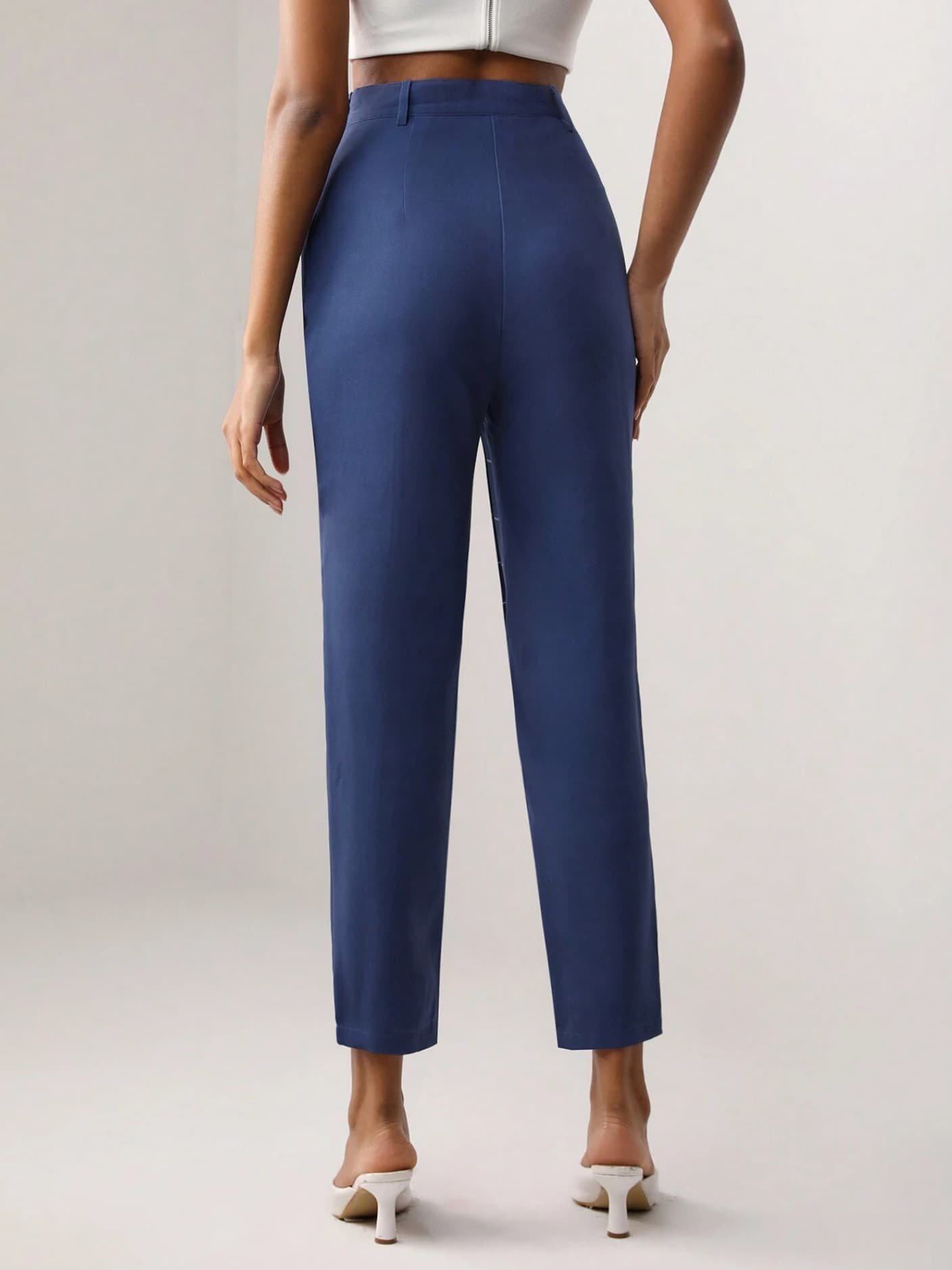 Back view of a model wearing blue high-waisted trousers and white heels from Keagan Roberson.