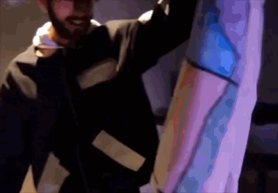 A person smiling and holding a large, colorful object or costume in a dimly lit environment.