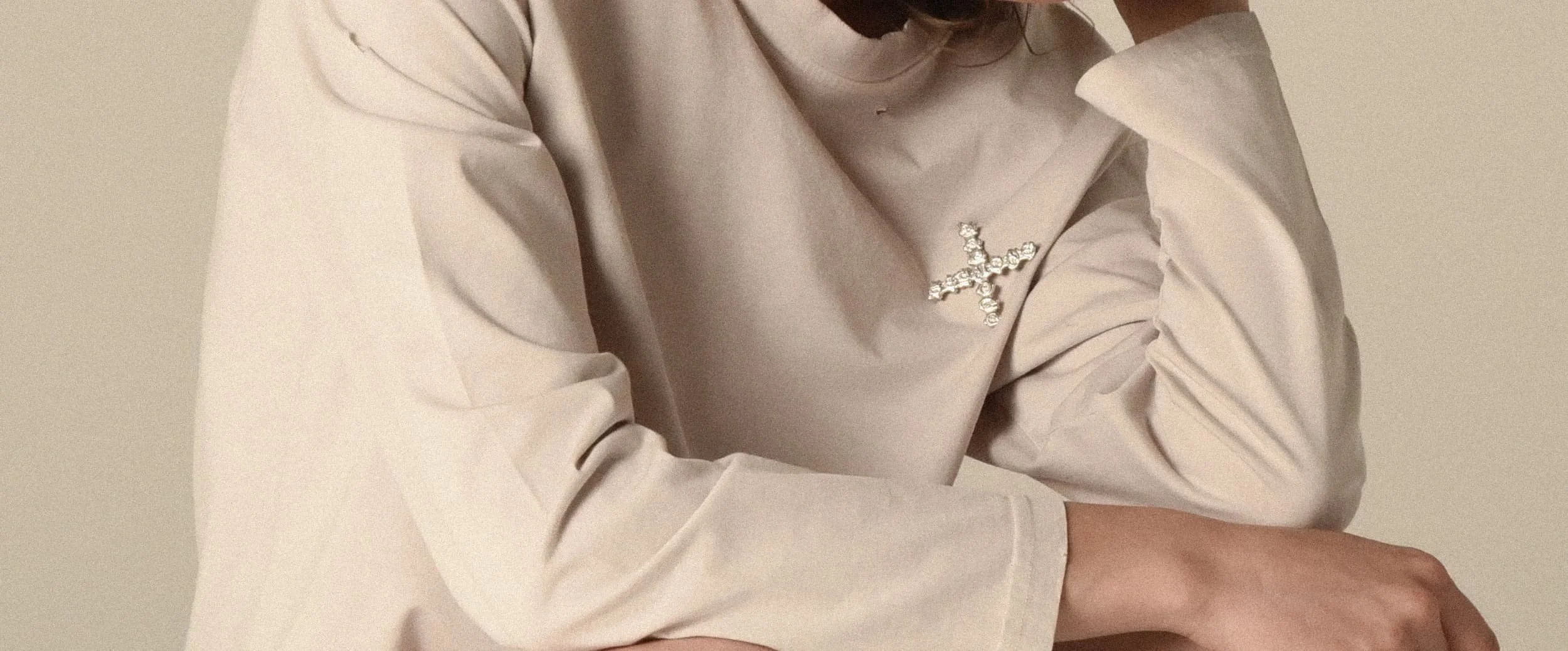 Close-up of a model wearing a beige long-sleeve shirt styled with a cross-shaped logo - designed in collaboration with Keagan Roberson.