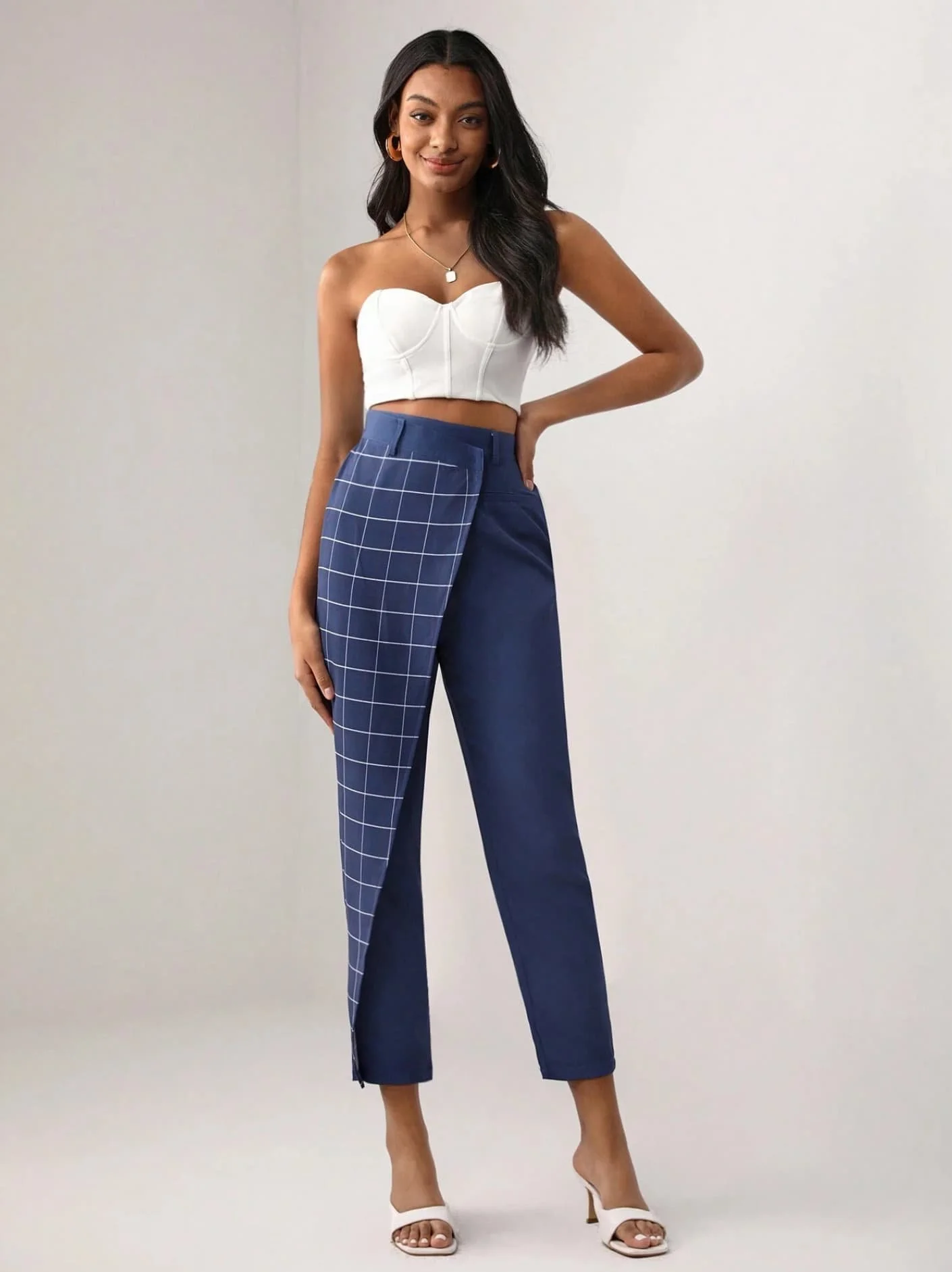 Model with dark hair wearing navy checkered trousers and a white strapless top from Keagan Roberson - modern styling captured in a minimalist studio.