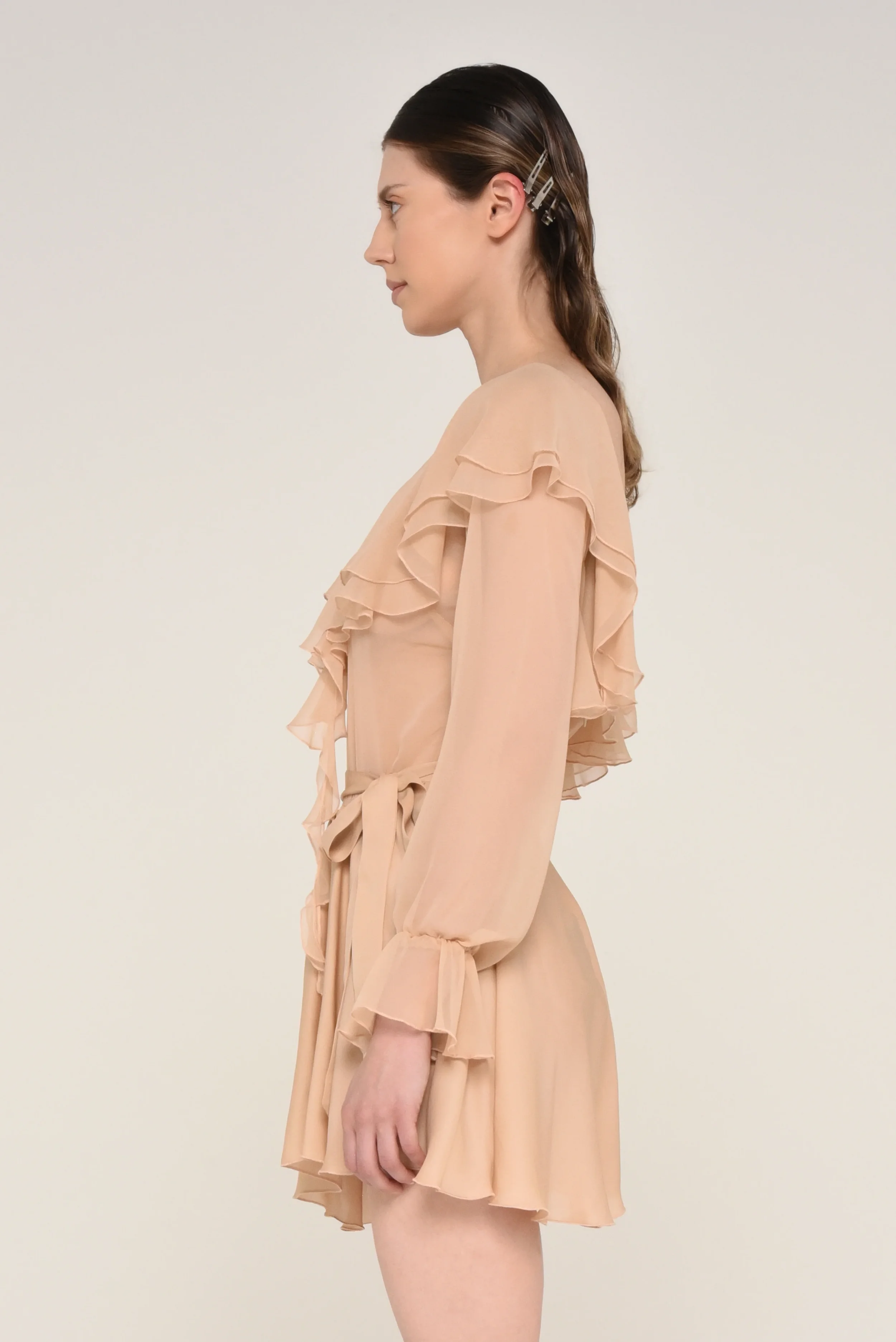 Side view of a model wearing a beige long-sleeve ruffled dress - designed in collaboration with Keagan Roberson.