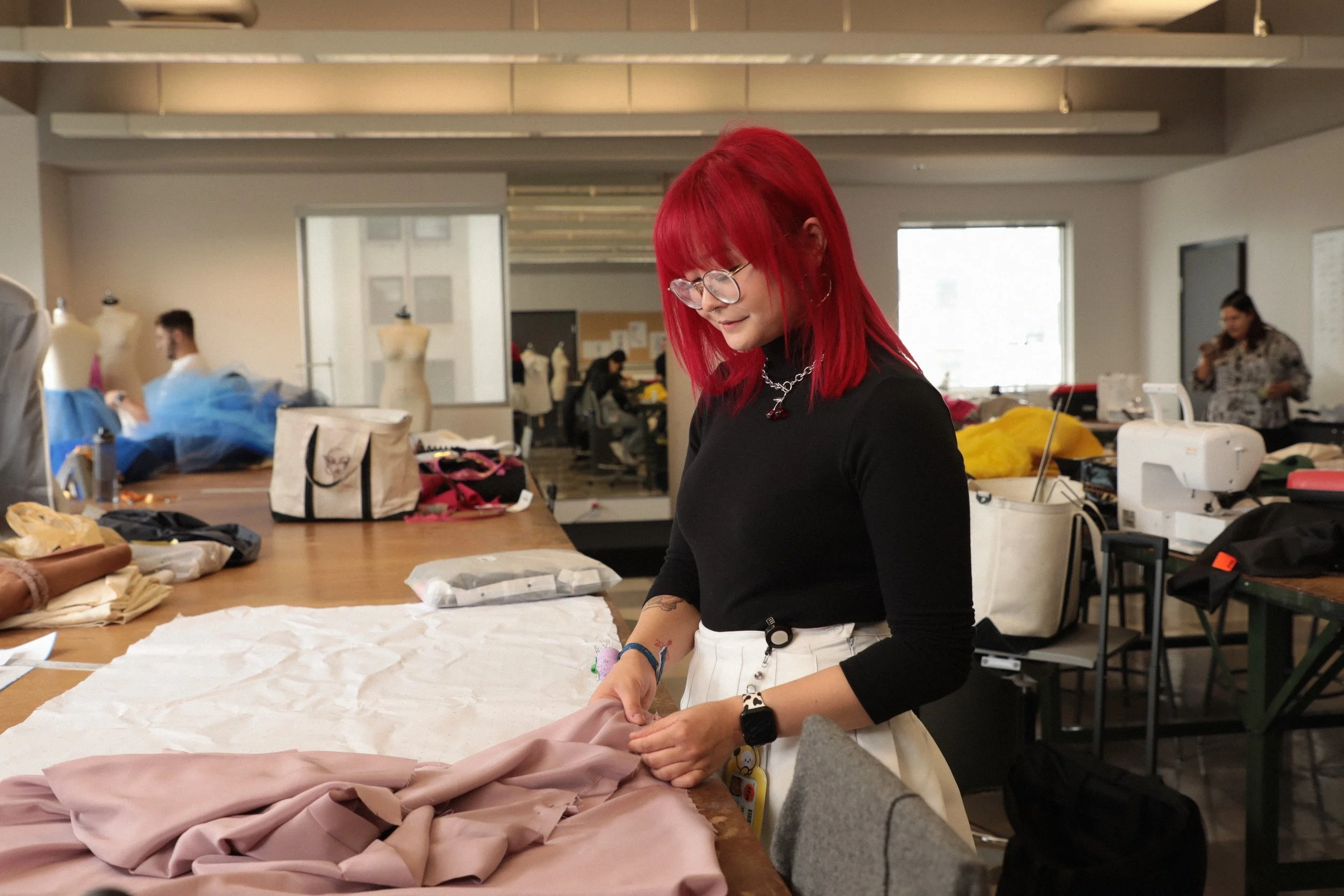 Monica Nakatani cutting fabric in a sewing studio filled with mannequins and tools.