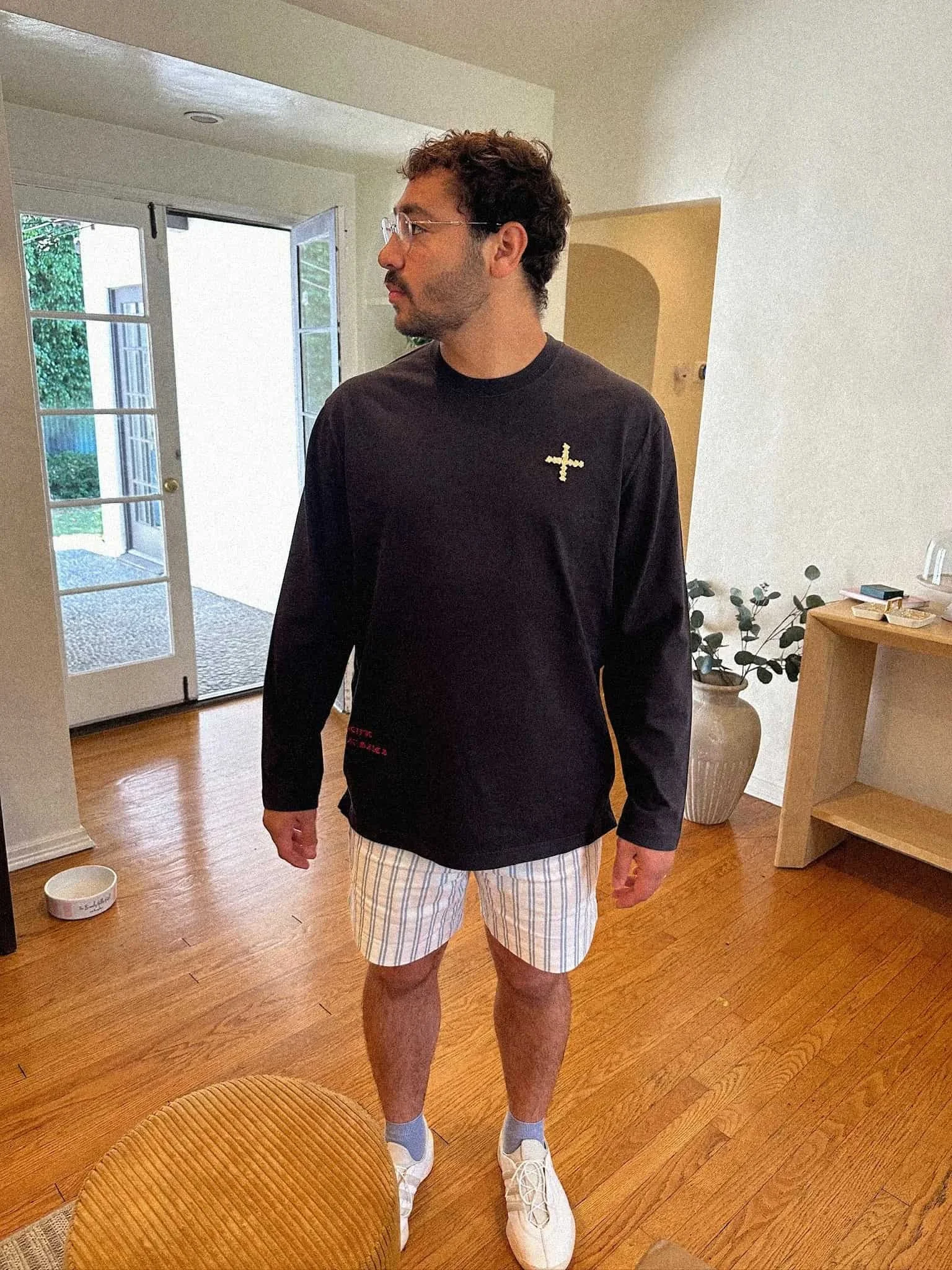 Keagan Roberson wearing a black long-sleeve shirt with a small cross emblem on the chest, paired with striped shorts and white sneakers.
