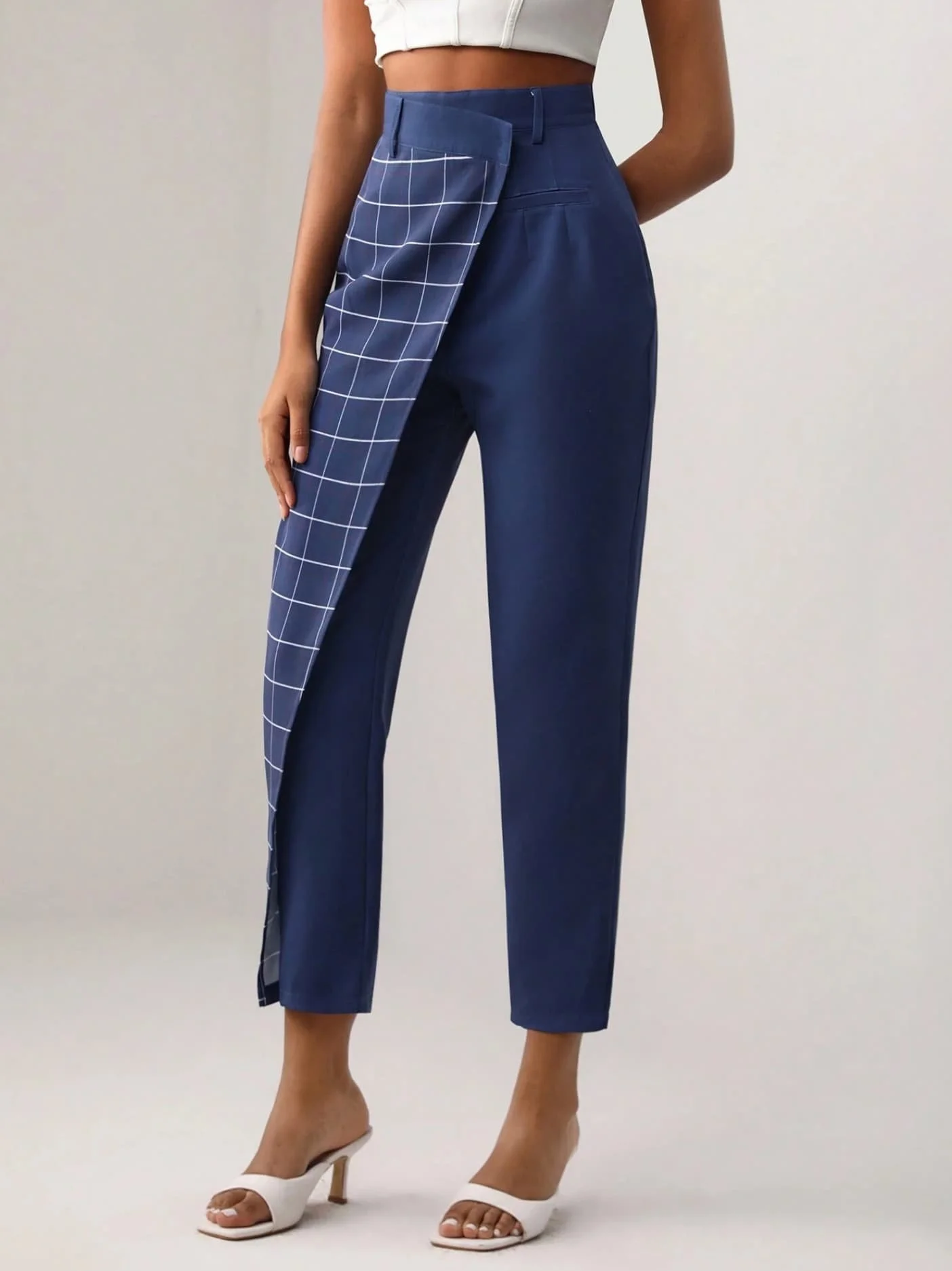 Model wearing blue tailored trousers with plaid detailing and a cropped white top from Keagan Roberson - clean composition emphasizing contrast and structure.