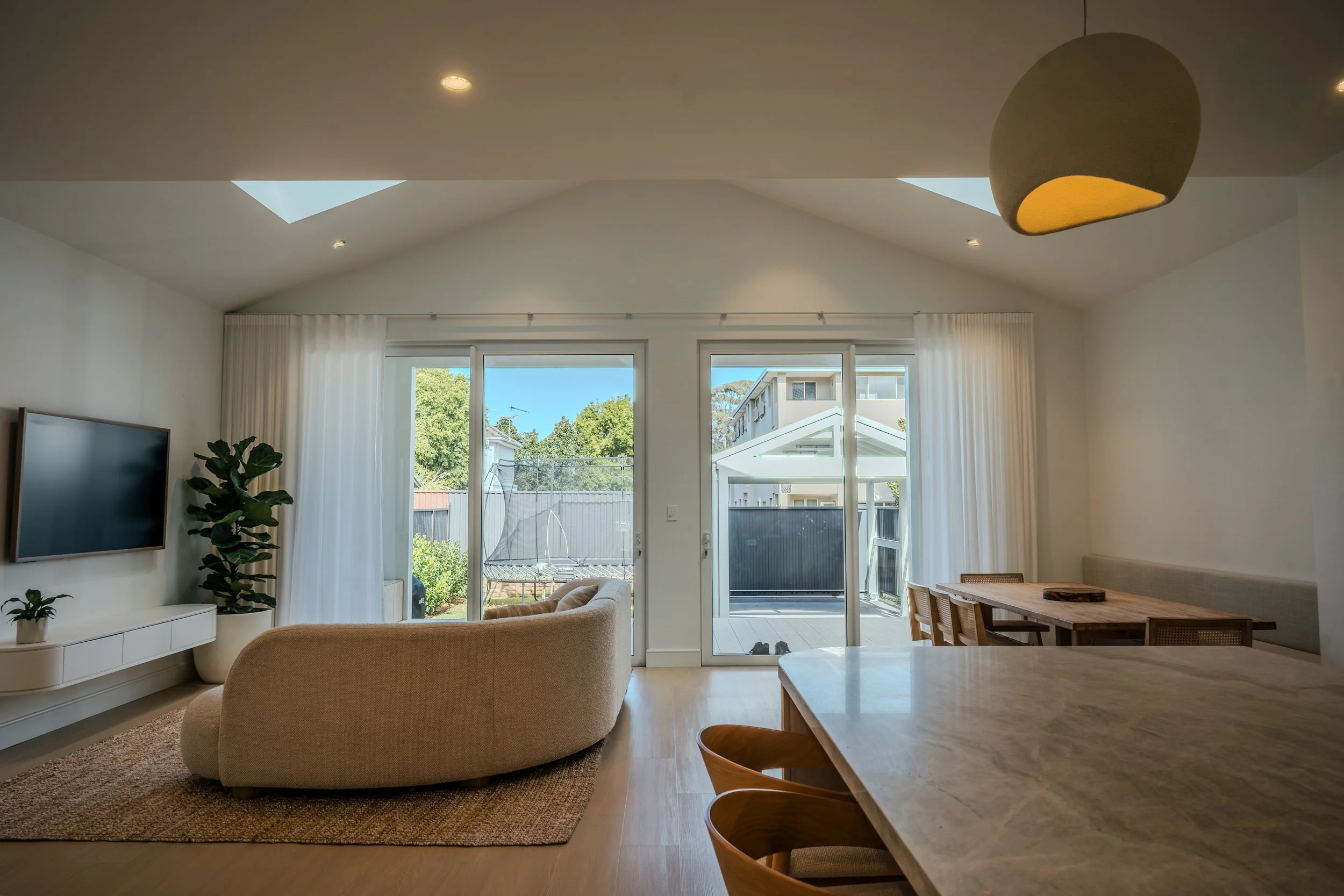 View from kitchen through modern living room to backyard with trampoline and carport