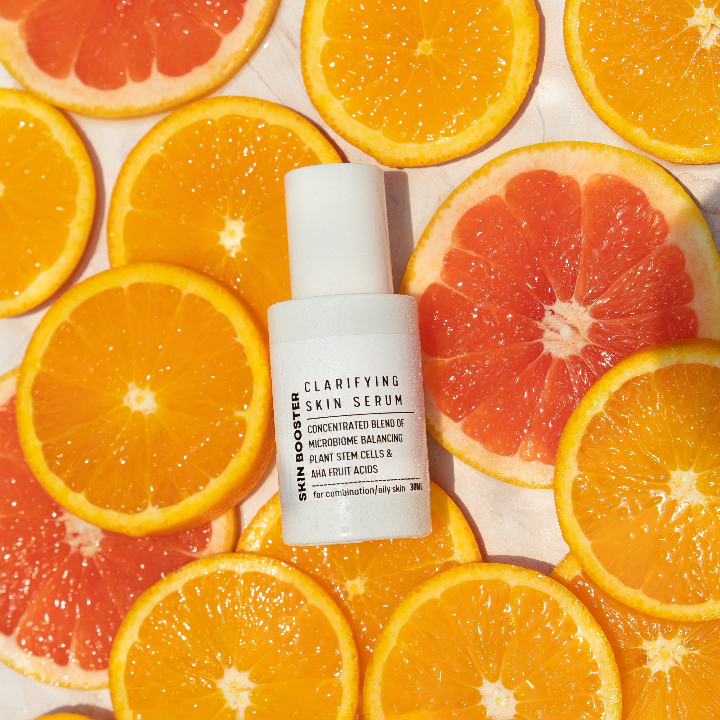 A white skincare bottle labeled 'Clarifying Skin Serum' surrounded by sliced oranges and grapefruits.