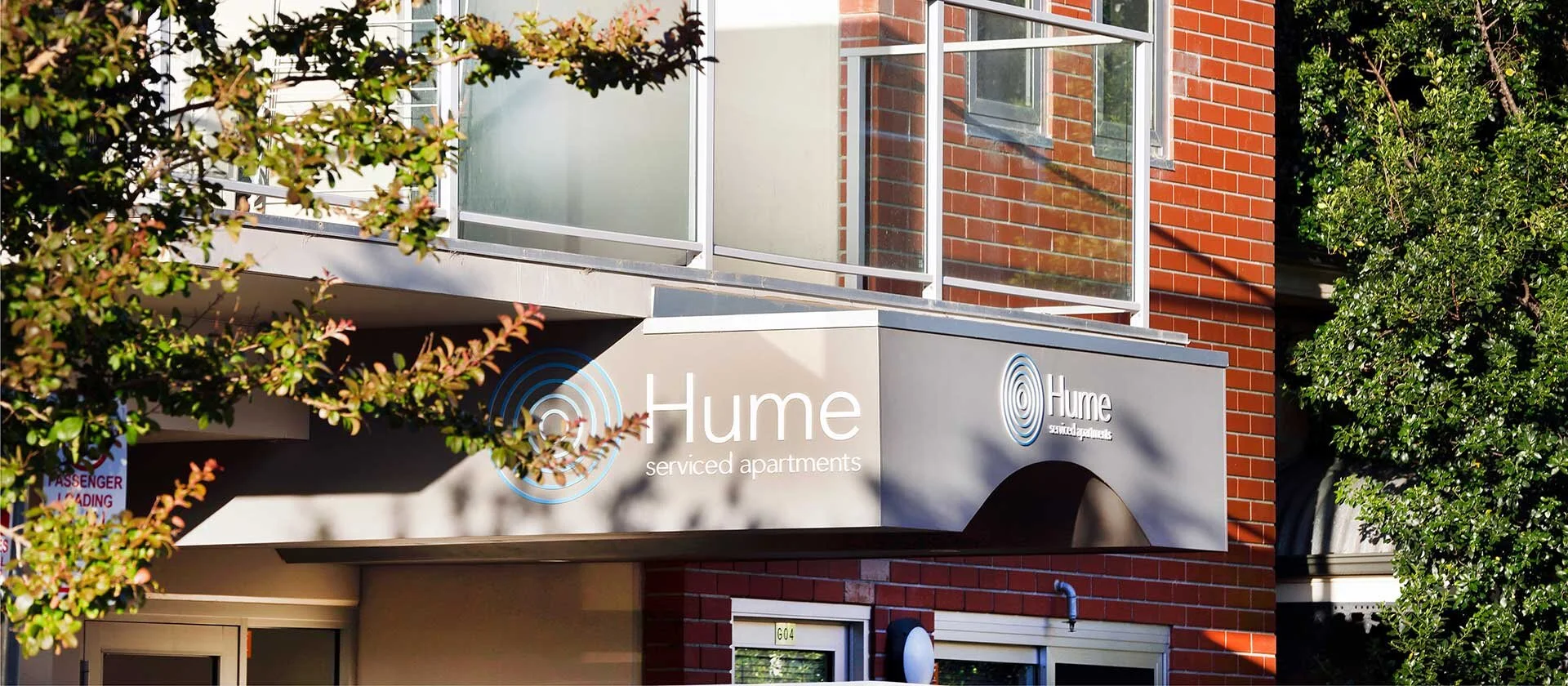 Hume serviced apartments exterior with signage, brick building, and tree branches.