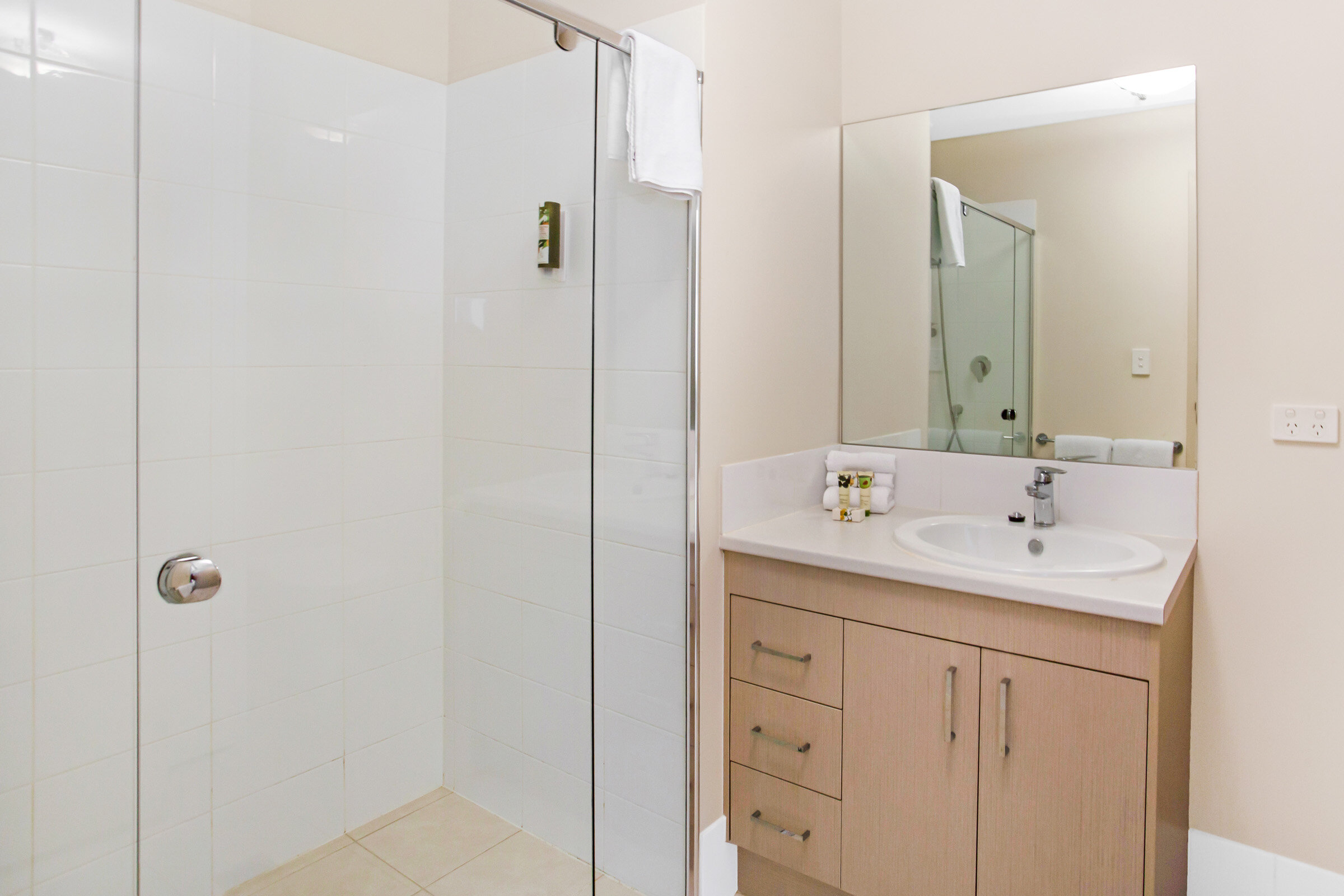 Modern bathroom with glass shower, wooden vanity with sink, mirror, and wall-mounted toiletries.
