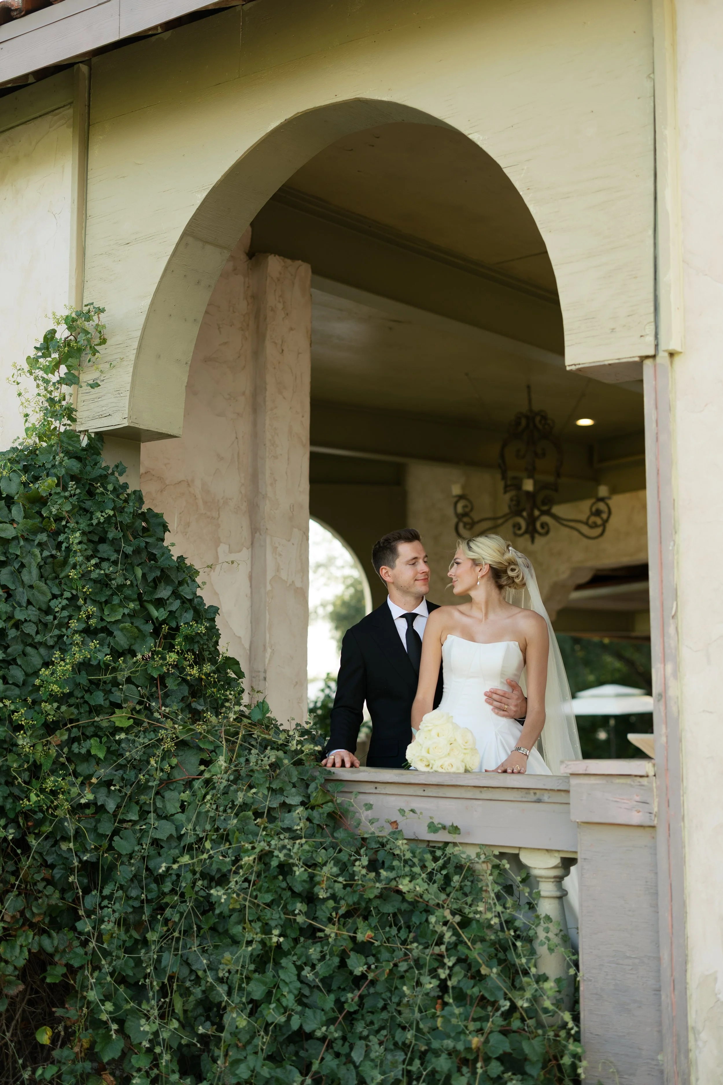 Wedding photo of bride in an off-the-shoulder satin dress and groom in a blue tux standing on the colorful stairs at the McNay Art Museum in San Antonio, Texas.