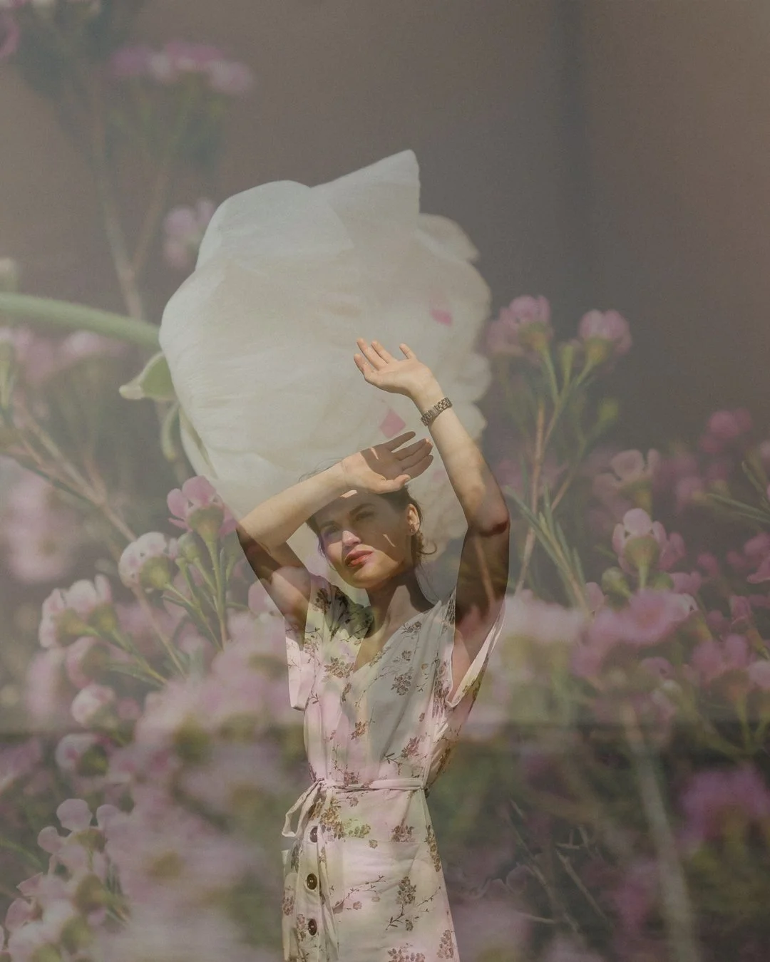 A woman wearing a floral dress holding a white pillow above her head, with a background of pink and purple flowers.