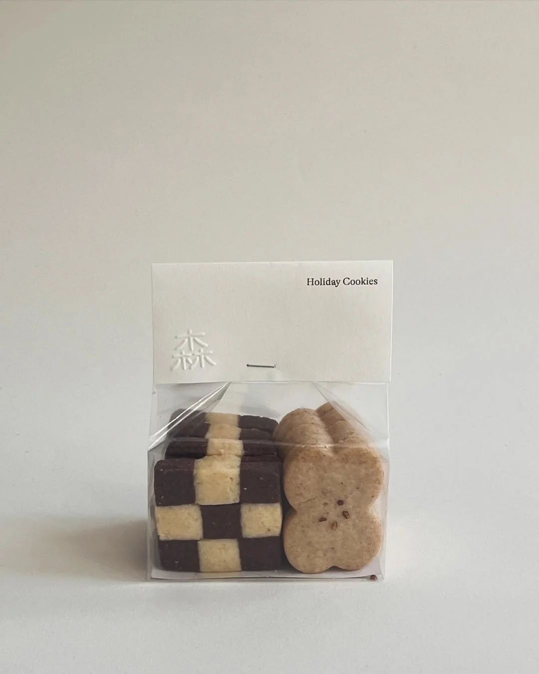 Clear plastic bag of holiday cookies labeled "Holiday Cookies" with checkerboard-patterned cookies and bear-shaped cookies inside.