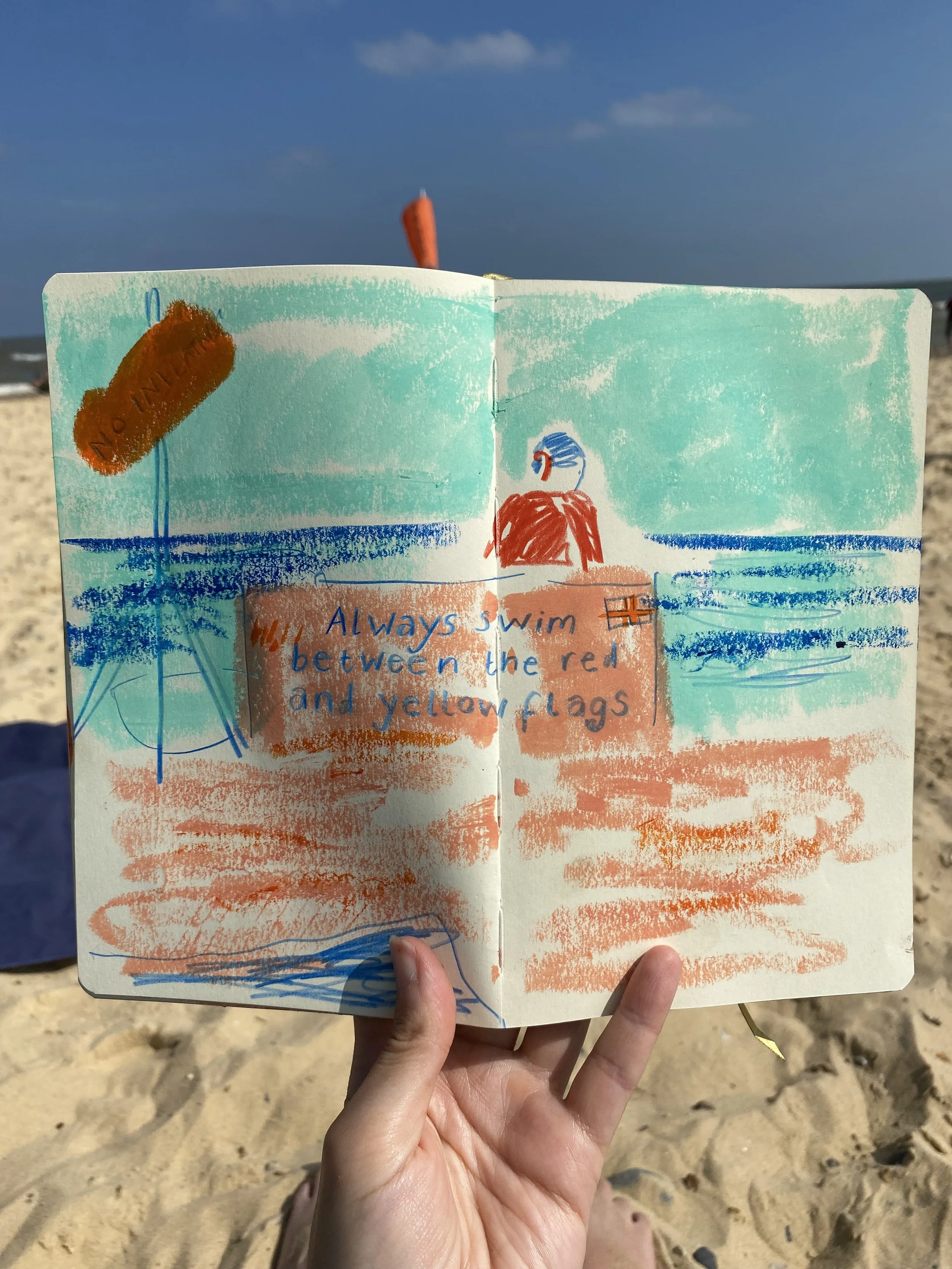 A sketchbook held by hand on a beach, showing a lifeguard station. With blue sky and sand visible in the background