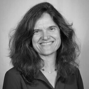Black and white portrait of a woman with shoulder-length wavy hair, smiling, wearing a dark top and a necklace.