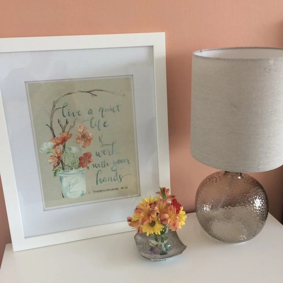 Nightstand with a lamp, flowers, and framed art print