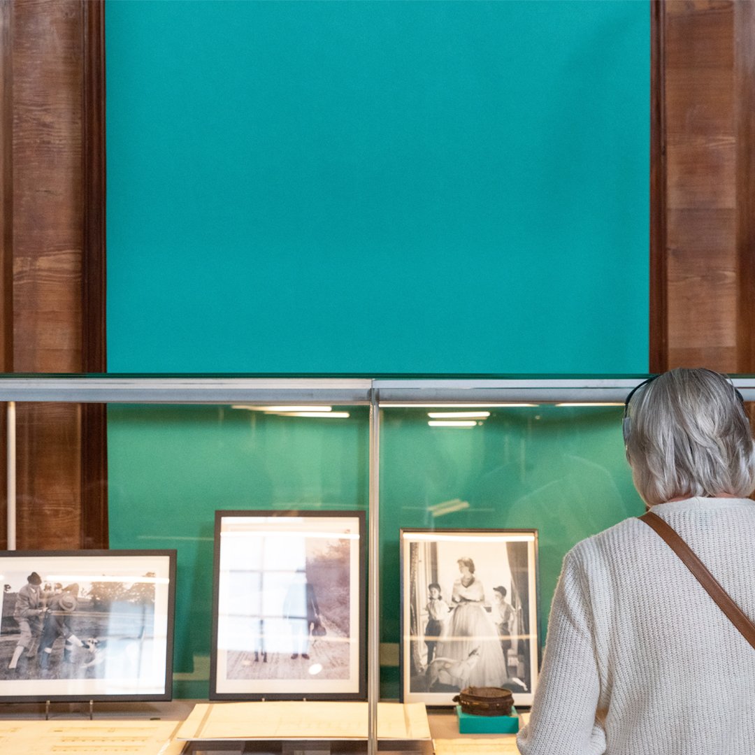 Visitor looking at archive photos in glass cabinet with turquoise banner behind it