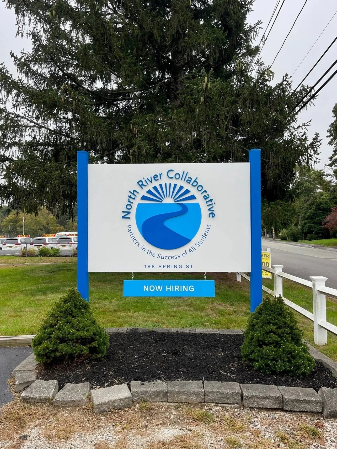 A blue and white sign with dimensional components, an address and a rider panel with message