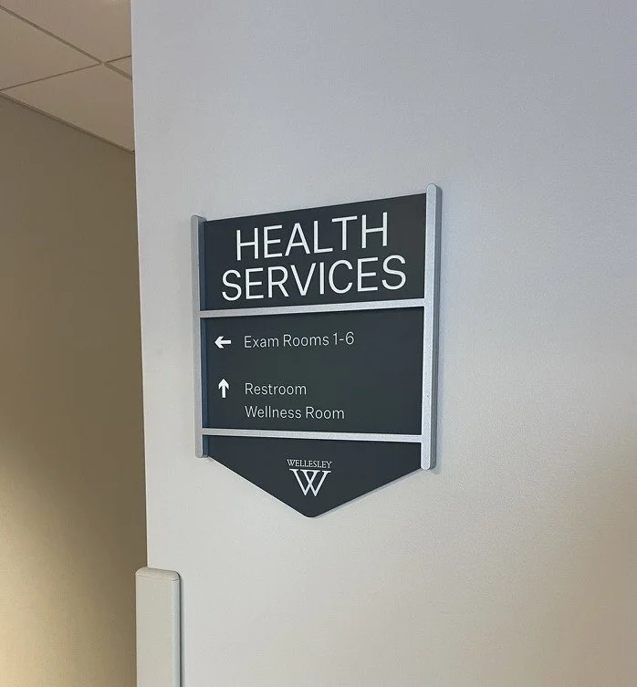 Sign for health services showing directions to exam rooms 1-6 and restrooms/wellness room at Wellesley.