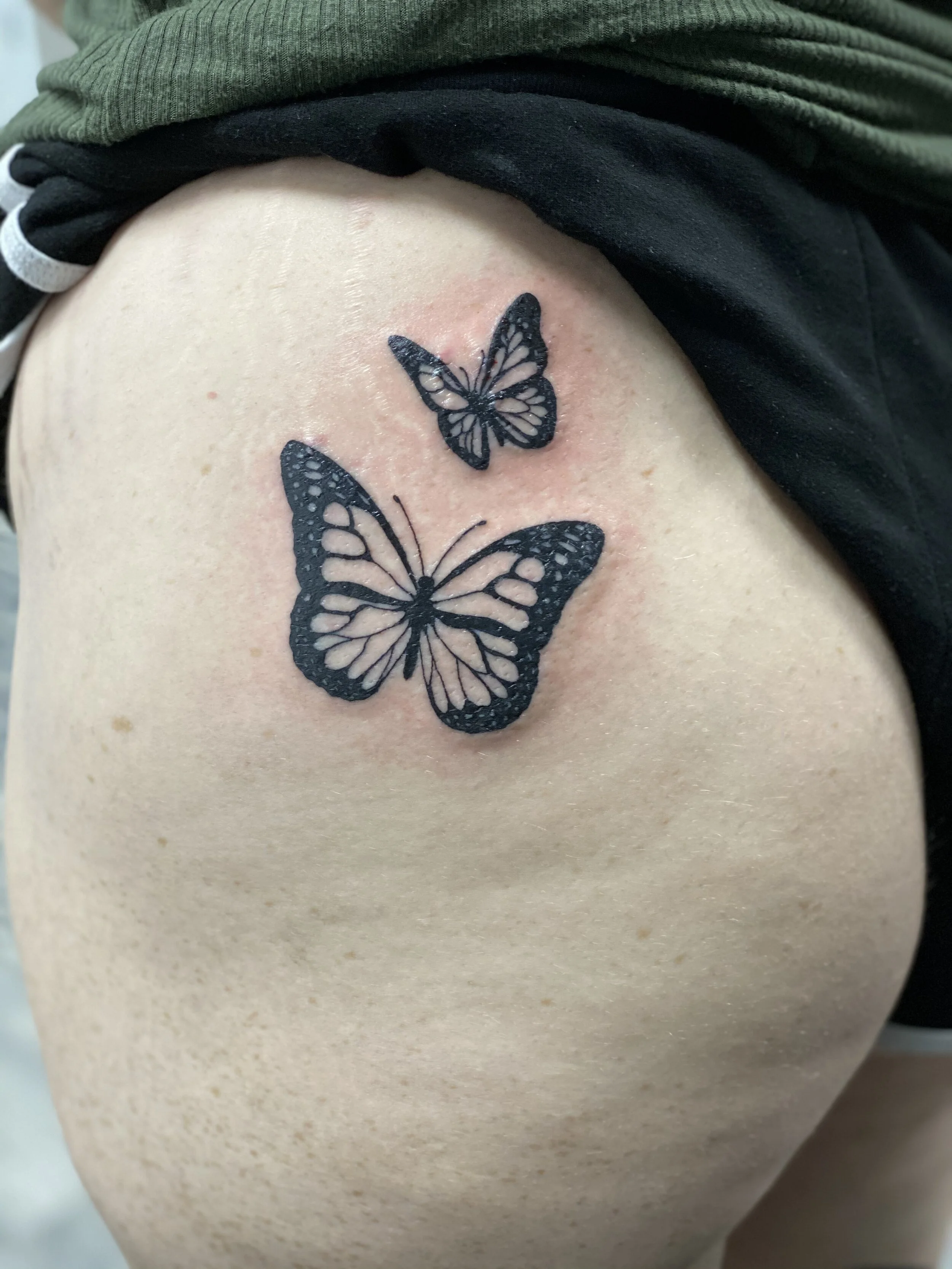 Close-up of a fresh butterfly tattoo on a person's side, featuring two black and white butterflies with detailed wings.