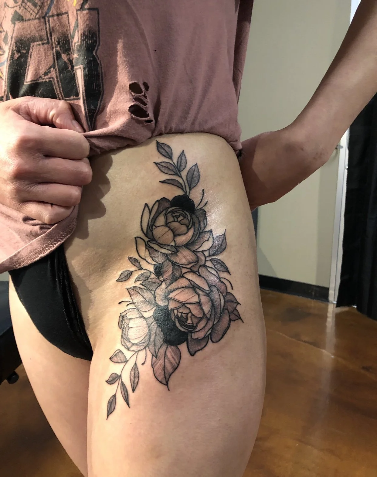 Tattoo of two large roses with leaves on the upper thigh of a person.