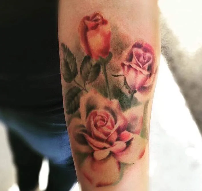 Tattoo of four pink and orange roses on a person's upper arm.