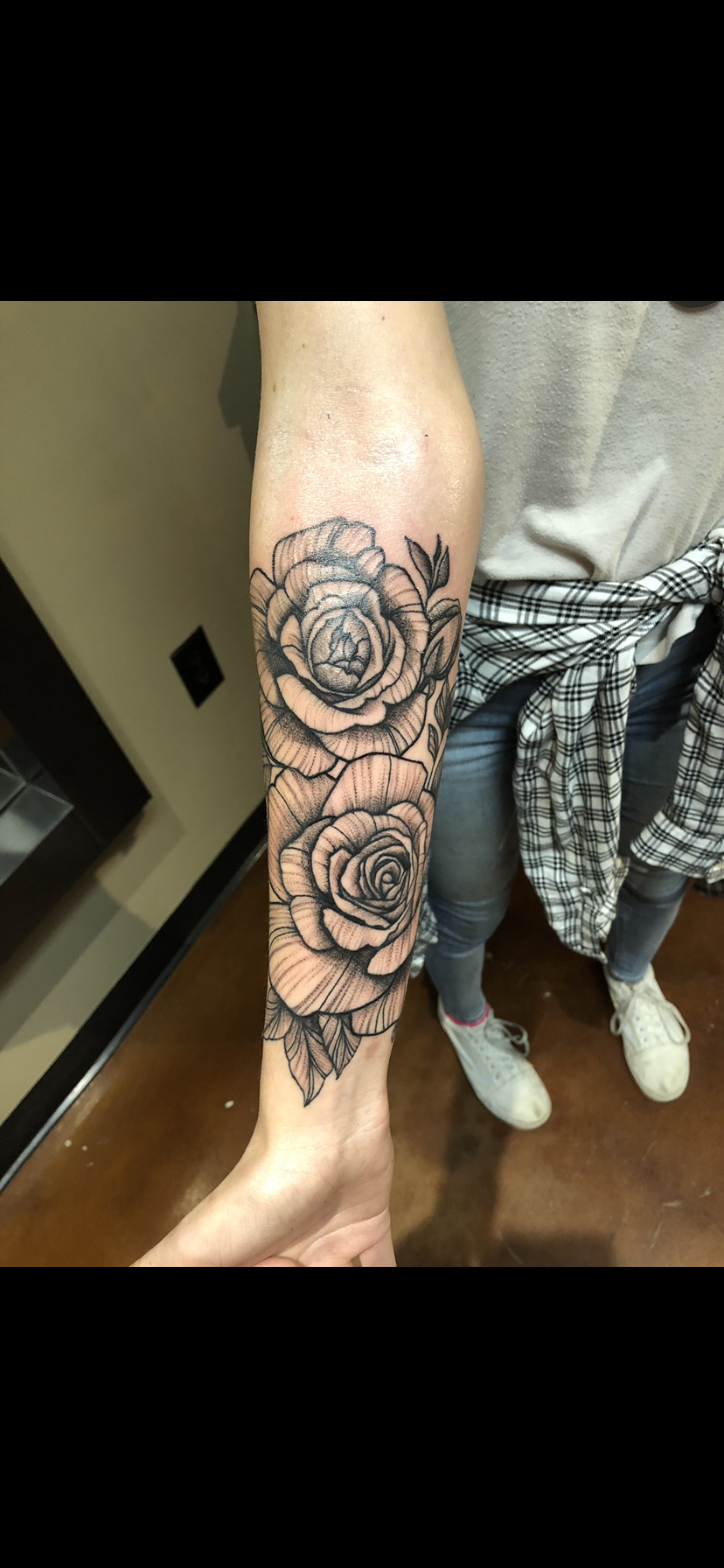 A person's arm with a black and gray floral tattoo featuring large roses and leaves.
