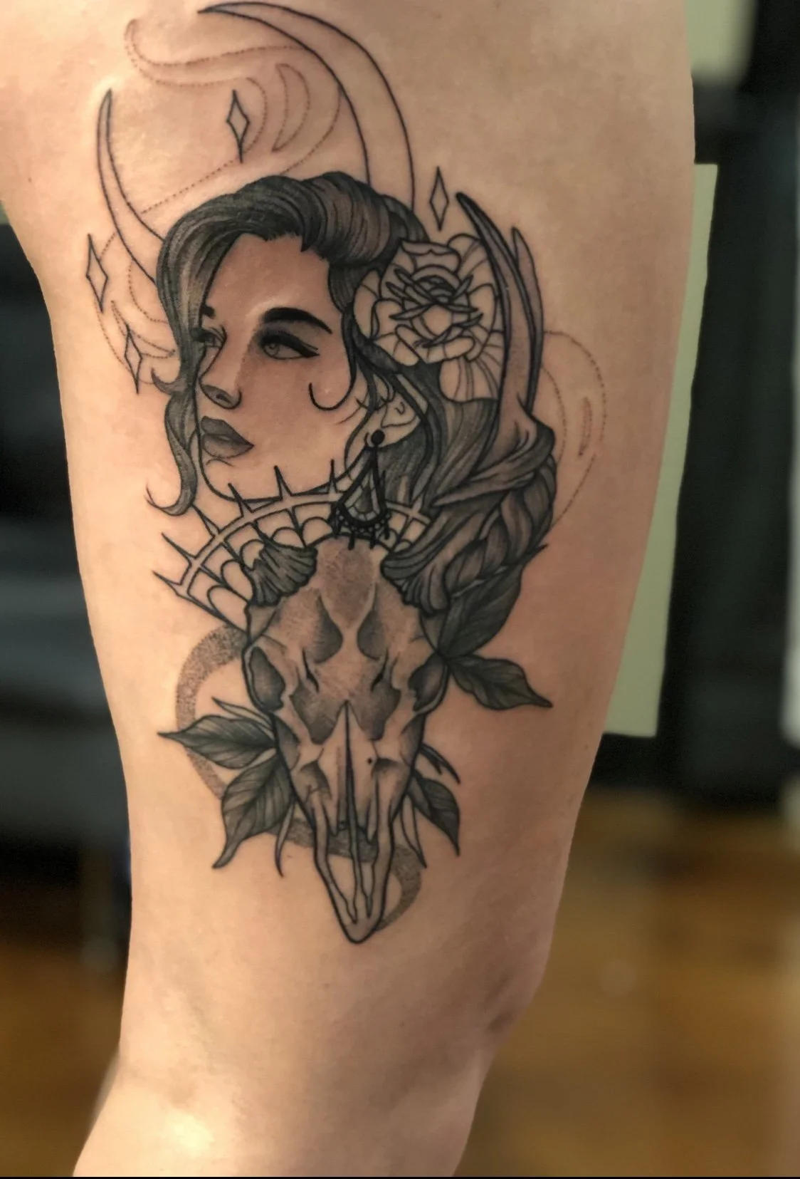 Tattoo of a woman's face with flowing hair, a rose, a skull, and leaves, all in black ink.