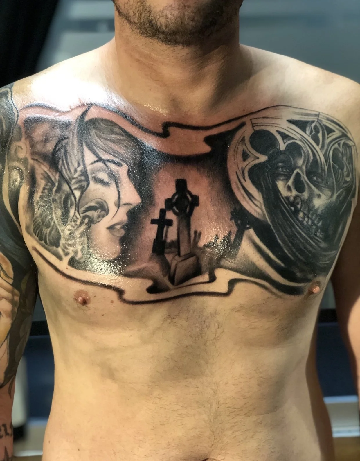 Black and gray tattoo of a woman with floral and ornamental elements on the left side of the chest and a skull with flowing hair on the right side, connected by a black line across the shoulders.