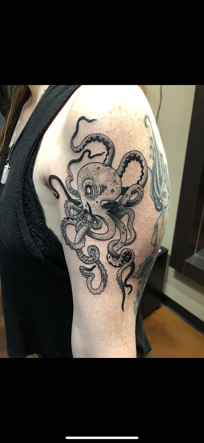 Black and gray tattoo of an octopus on a person's upper arm and shoulder.