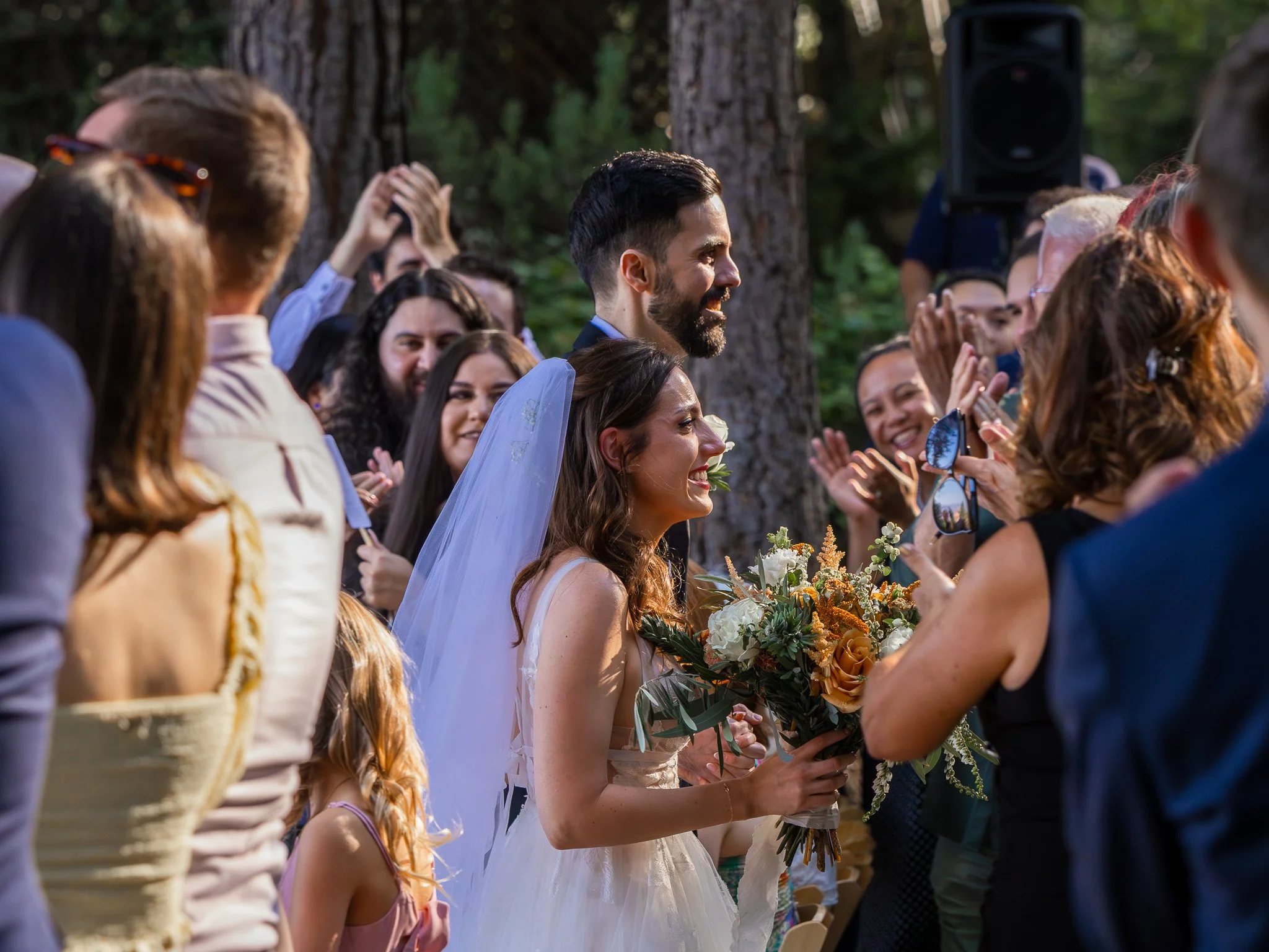 Bride and groom smiling amidst guests at an outdoor wedding