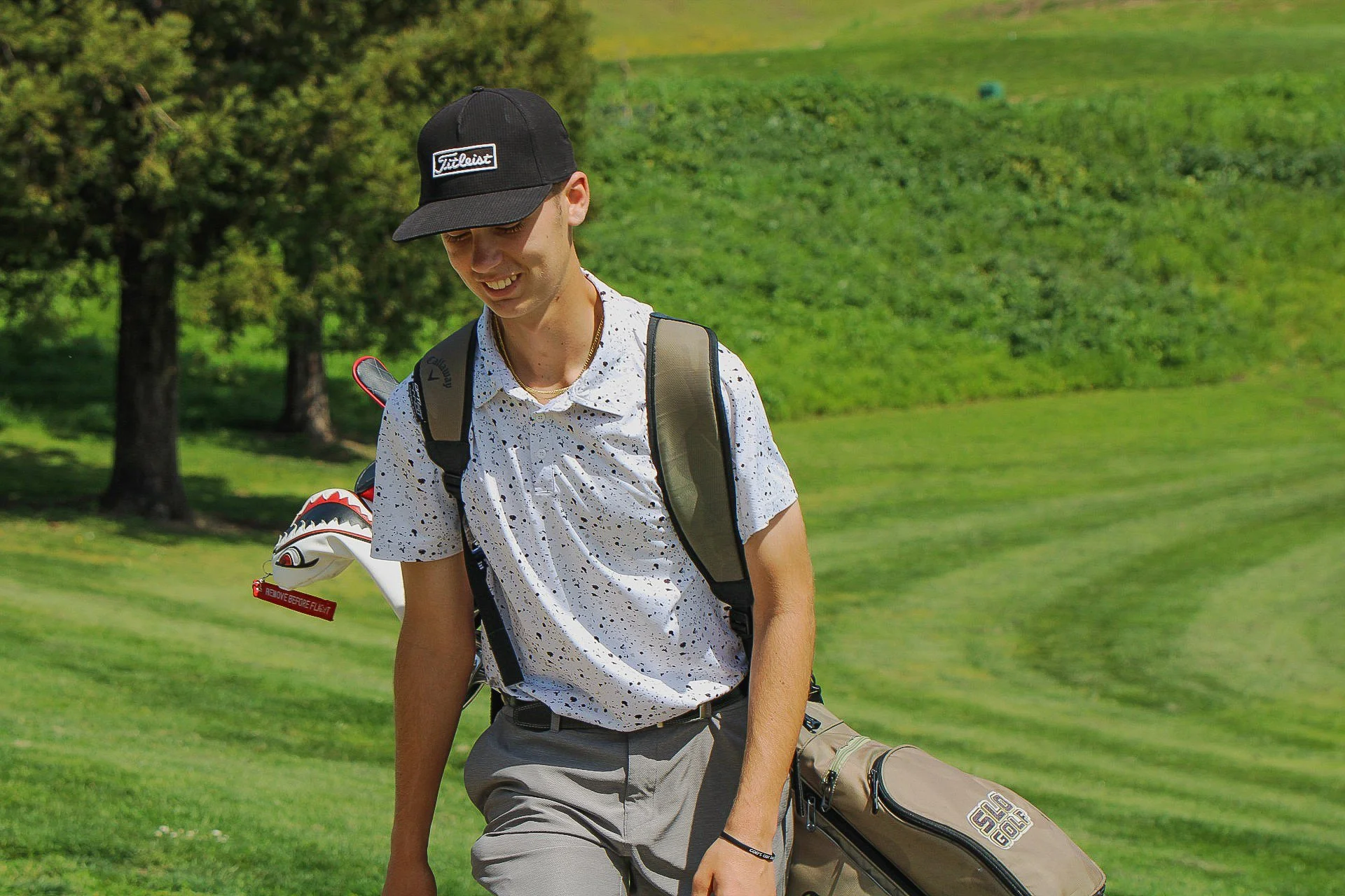 A young man dressed in golf attire walking on a golf course, carrying a golf bag.