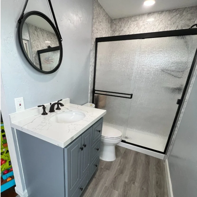 acrylic shower, luxury vinyl plank flooring, grey solid wood vanity with white quartz top, matte black fixtures