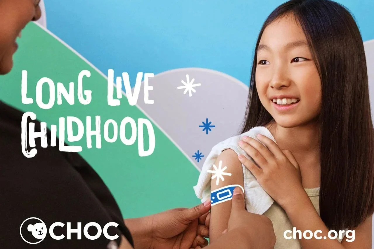 A young girl receives a vaccination injection in her upper arm during a medical visit, with a healthcare professional administering the shot. The background has a colorful, geometric design with the message 'Long Live Childhood' and logos for CHOC an