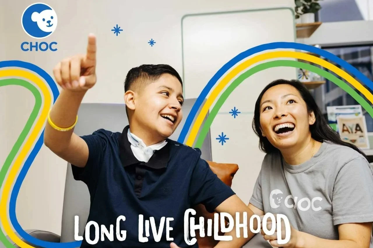 A smiling woman and boy sitting together in an indoor setting, with colorful rainbow and snowflake graphics and the words 'Long Live Childhood' on the image. The woman is wearing a gray "CHOC" T-shirt, and the boy is wearing a navy blue shirt. There 