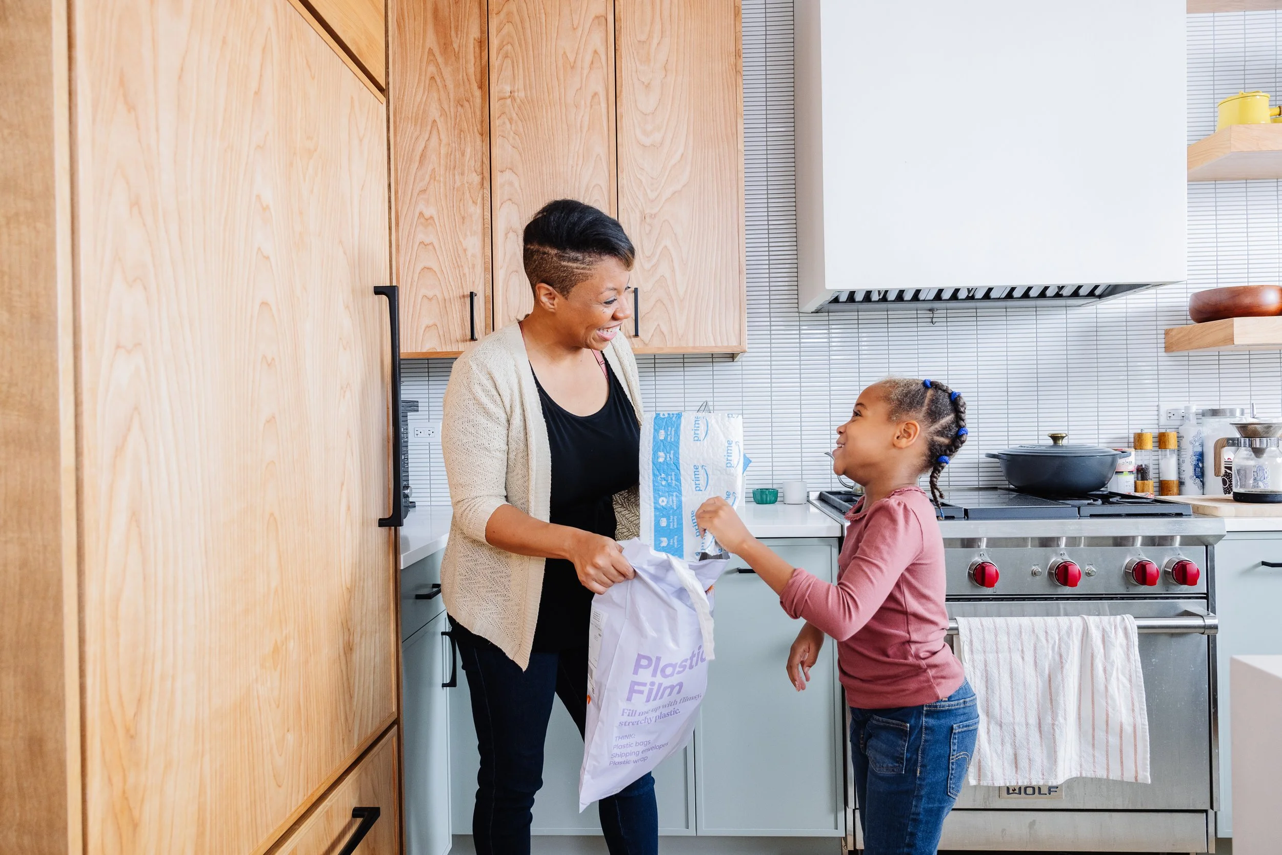 A woman and a young girl exchanging a gift in a modern kitchen, smiling at each other.